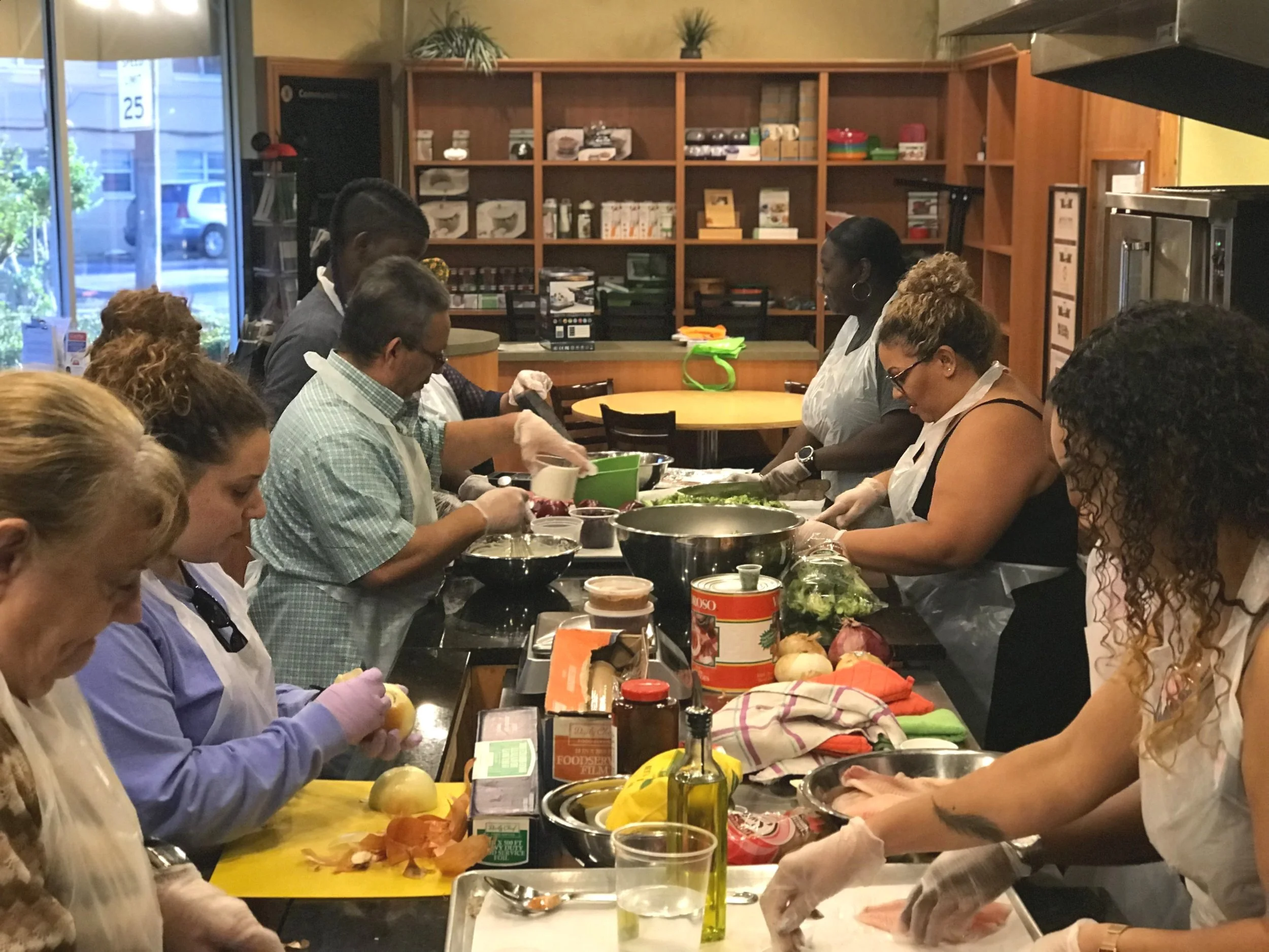 Group of people cooking together in a cooking class, preparing food with various fresh ingredients and utensils on the counter.