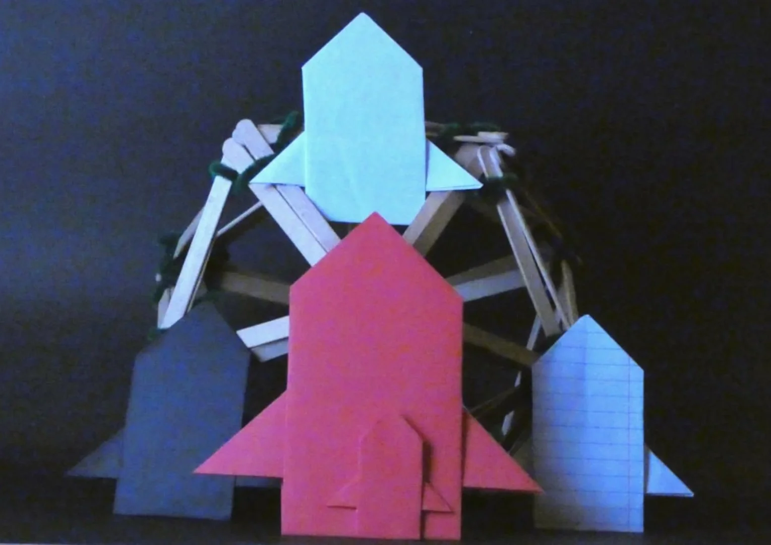 Colorful paper and wooden rocket and spaceship models against a dark background.