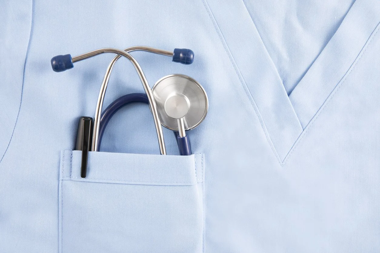 Close-up of a light blue medical uniform with a pocket containing a stethoscope and a black pen.