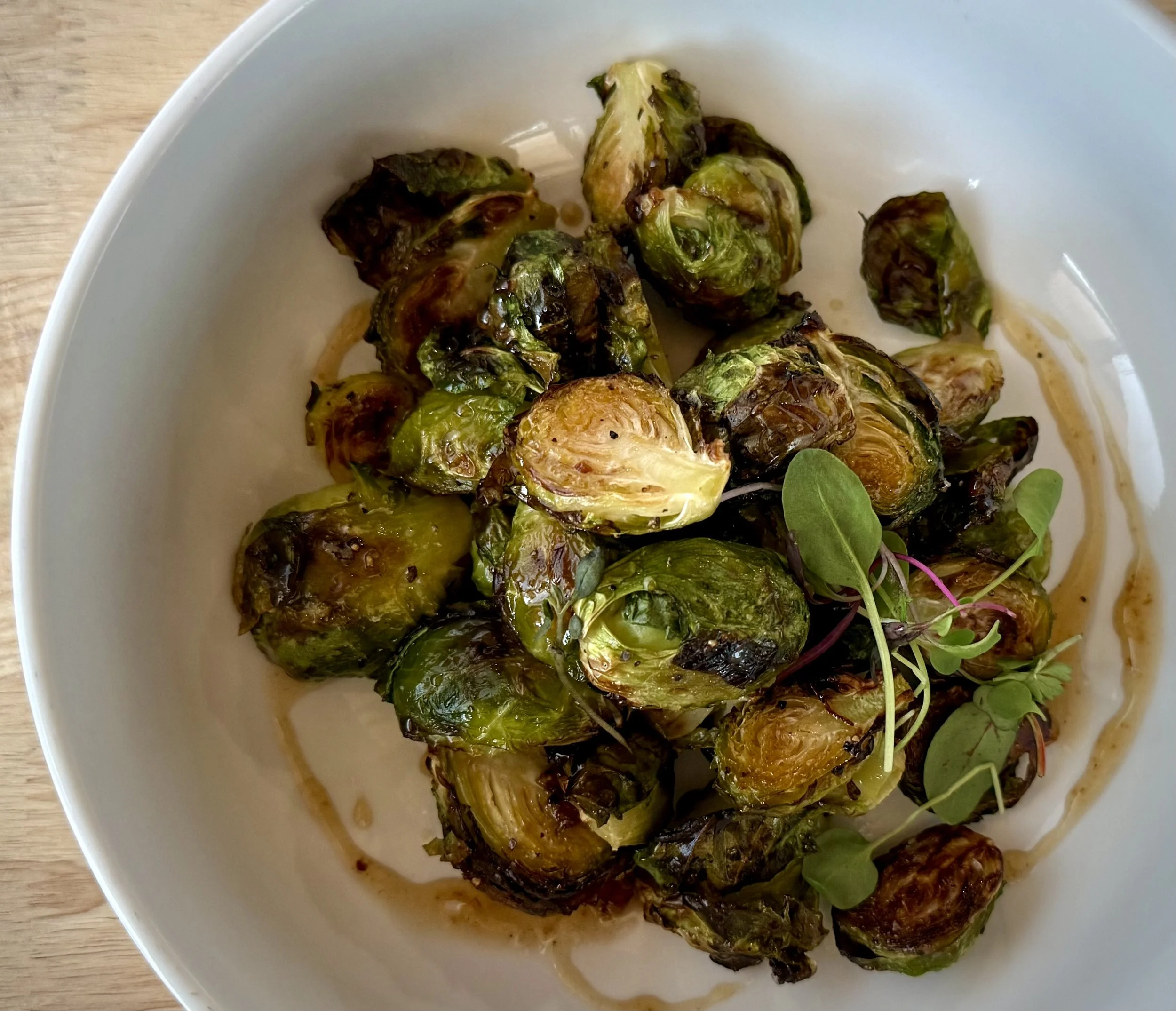 Roasted Brussels sprouts on a white plate, garnished with microgreens, with some oil or sauce around them.