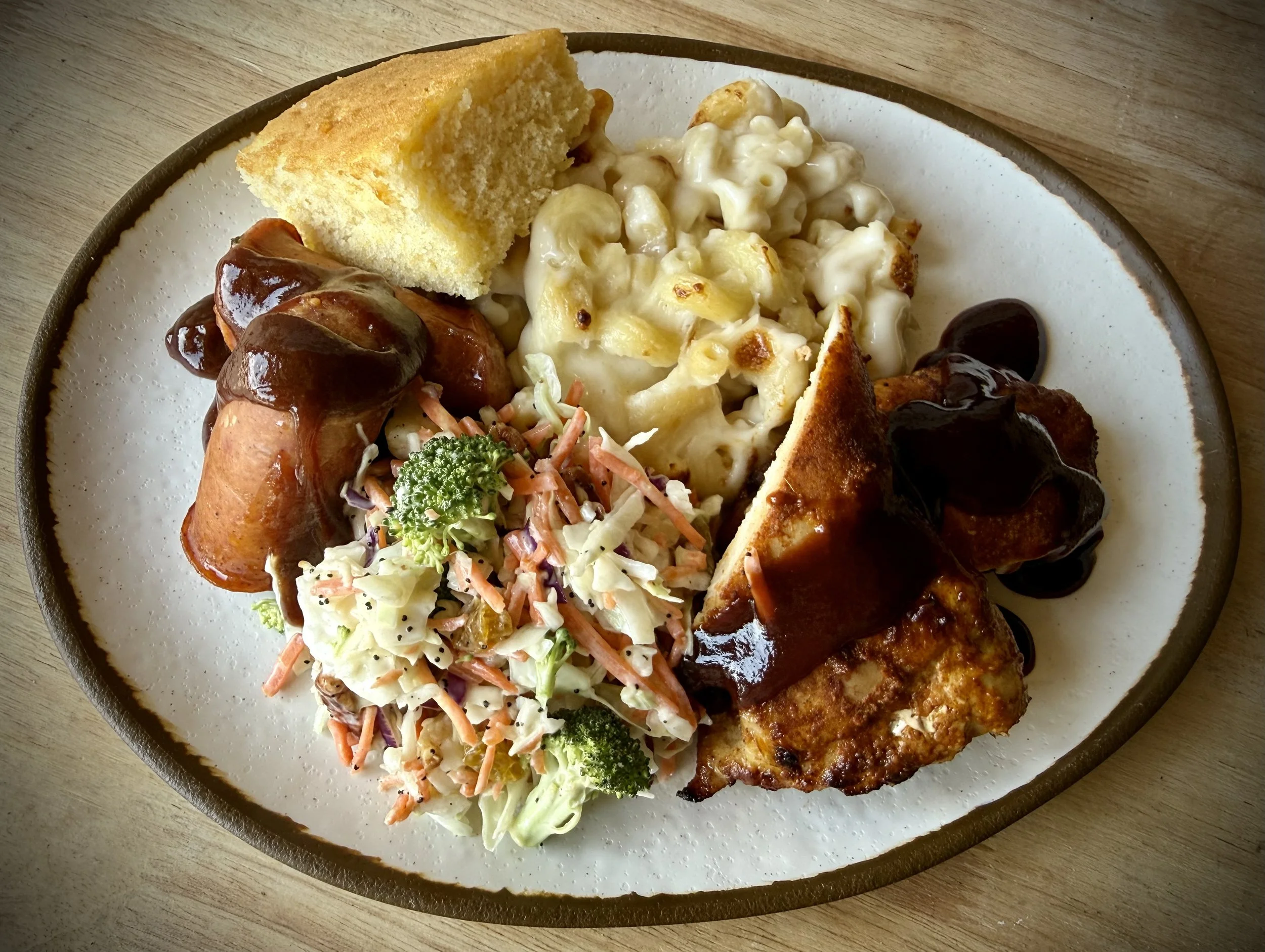 A plate of comfort food including mashed potatoes with gravy, macaroni and cheese, a slice of cornbread, a small salad with broccoli, coleslaw, and roast meat with gravy.