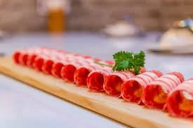 Thin slices of cured meat arranged on a wooden board, garnished with a sprig of parsley.