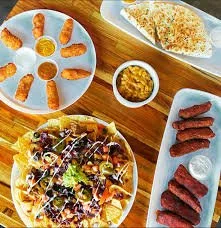 Assorted dishes including fried chicken wings, fried corn, barbecue ribs, a salad, corn on the cob, and sweet potato fries on a wooden table.