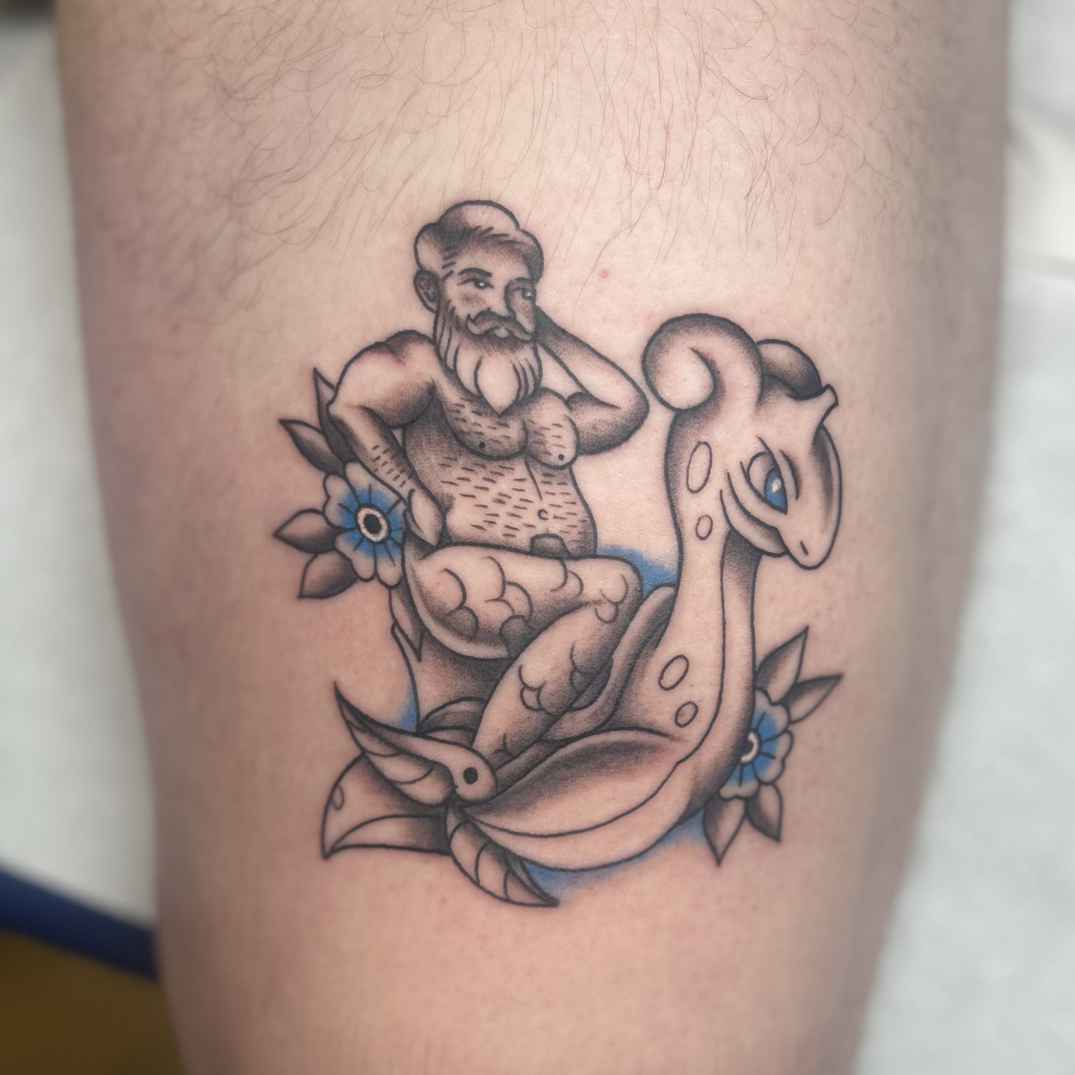 Black & gray custom LGBTQIA‑inspired Lapras Pokémon tattoo, blue eye accents and flowers
