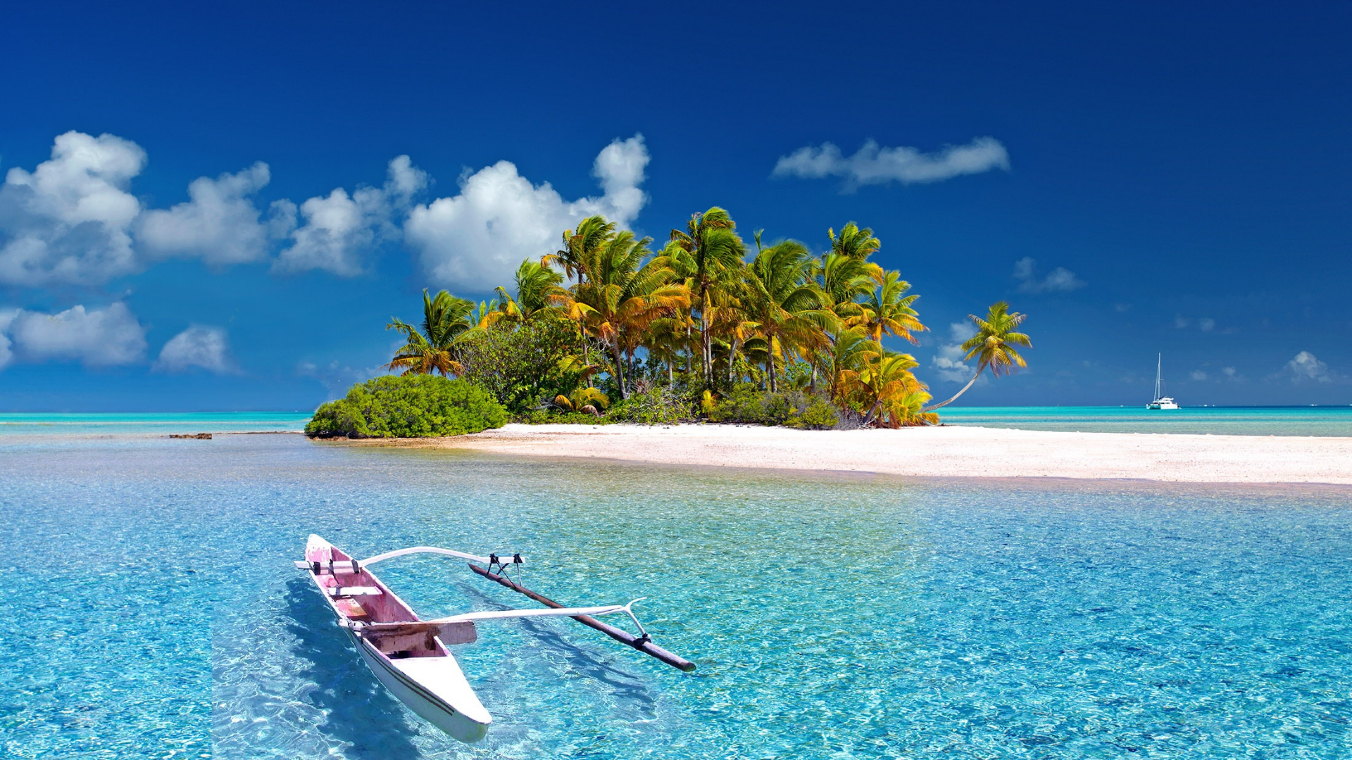 A tropical island with a sandy beach, lush green trees, palm trees, a boat in the clear turquoise water, and a sailboat in the distance under a blue sky with scattered clouds.
