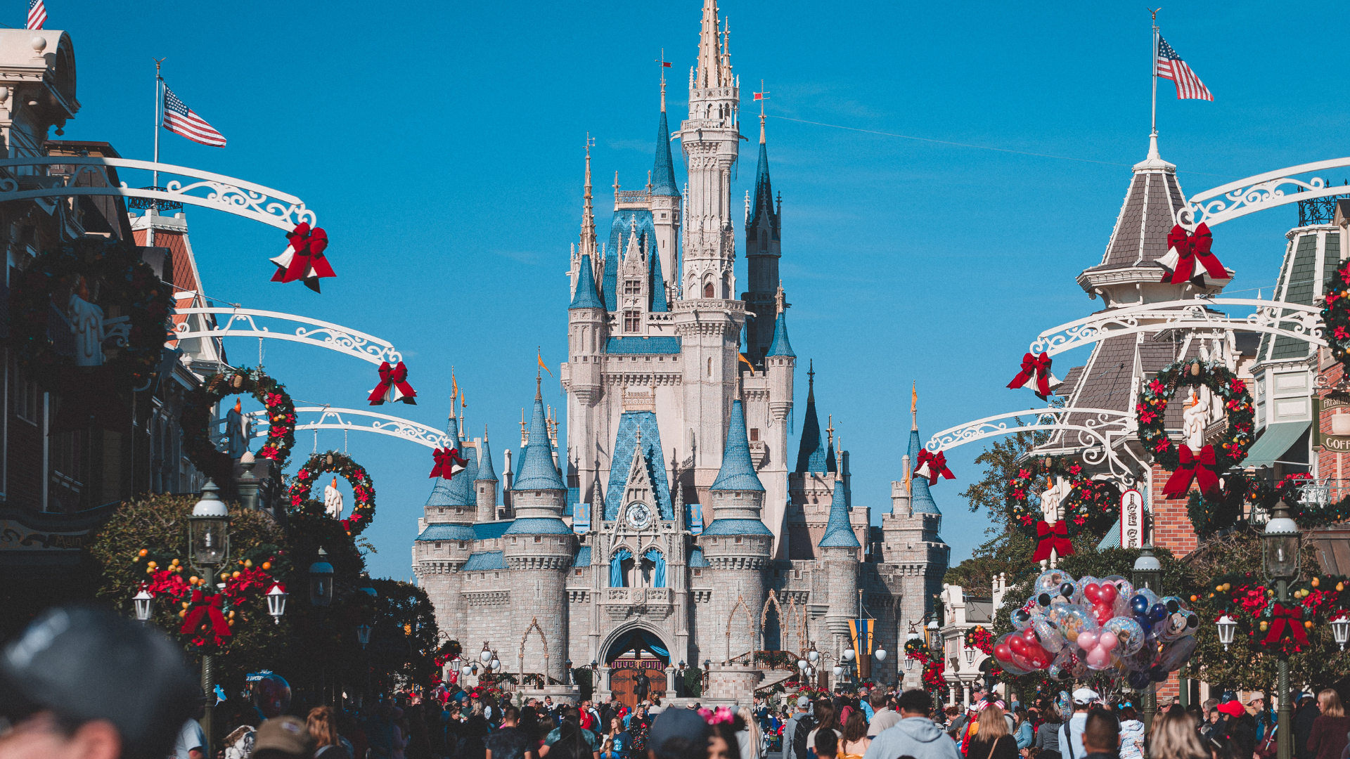 Cinderella Castle at Disney World decorated for Christmas with red bows, wreaths, and holiday ornaments, crowded with visitors on a sunny day.