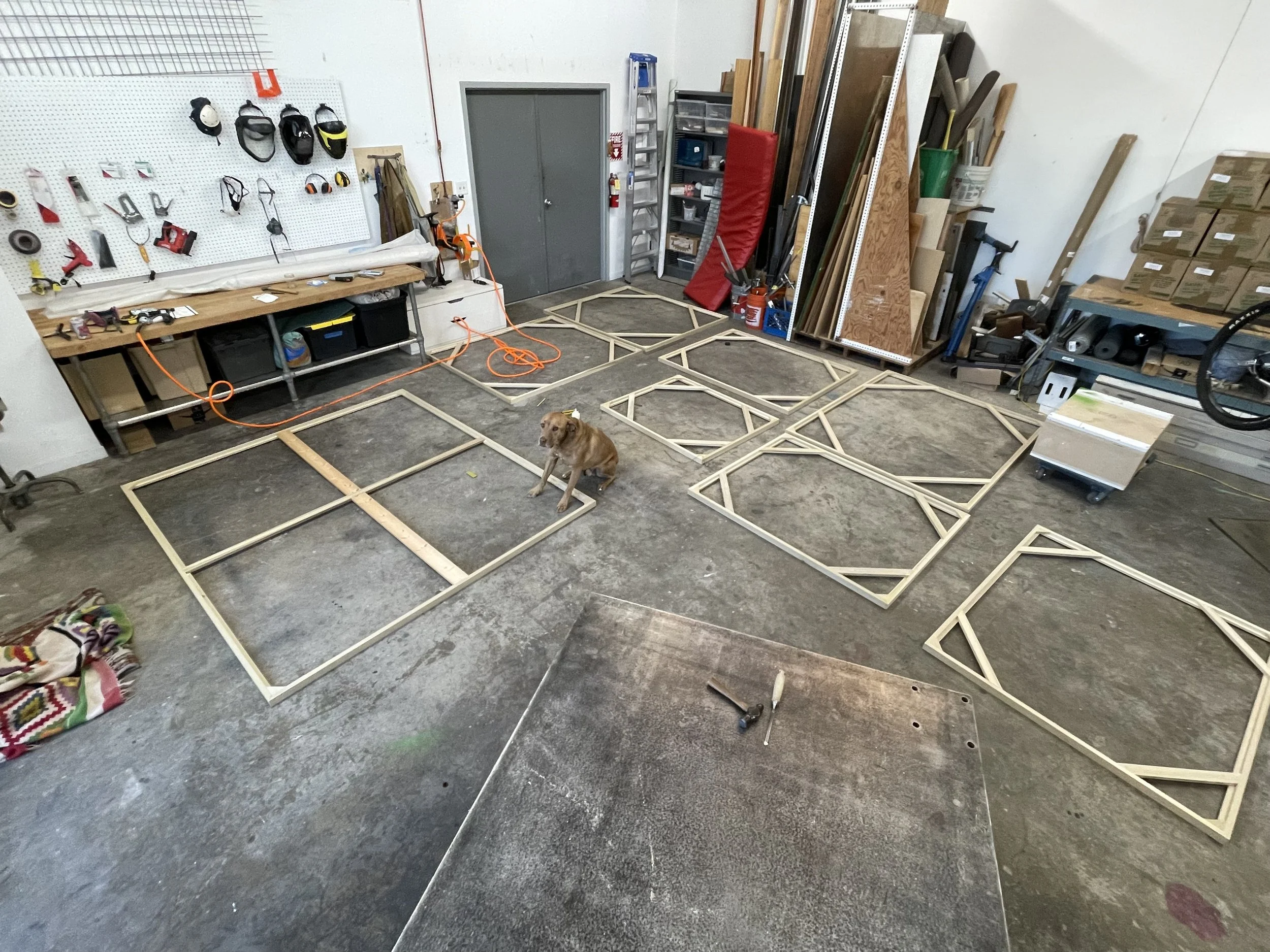 Workshop with wooden frames on the floor, tools on a workbench, and a dog sitting in the center.