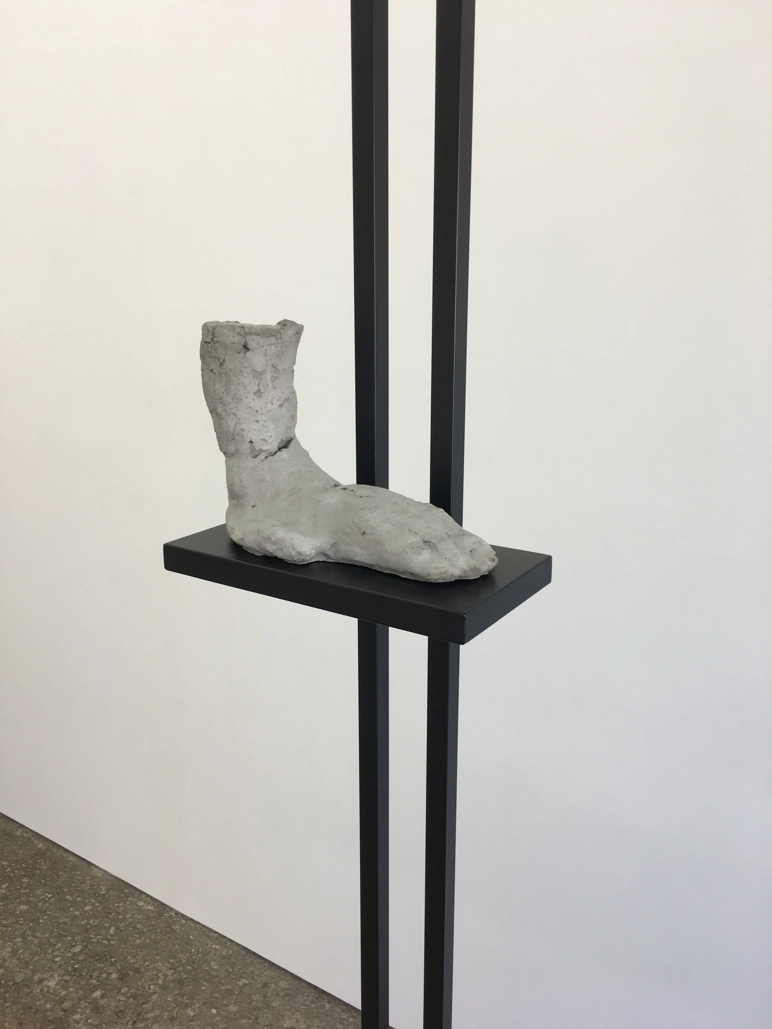 Concrete sculpture of a foot on a black pedestal