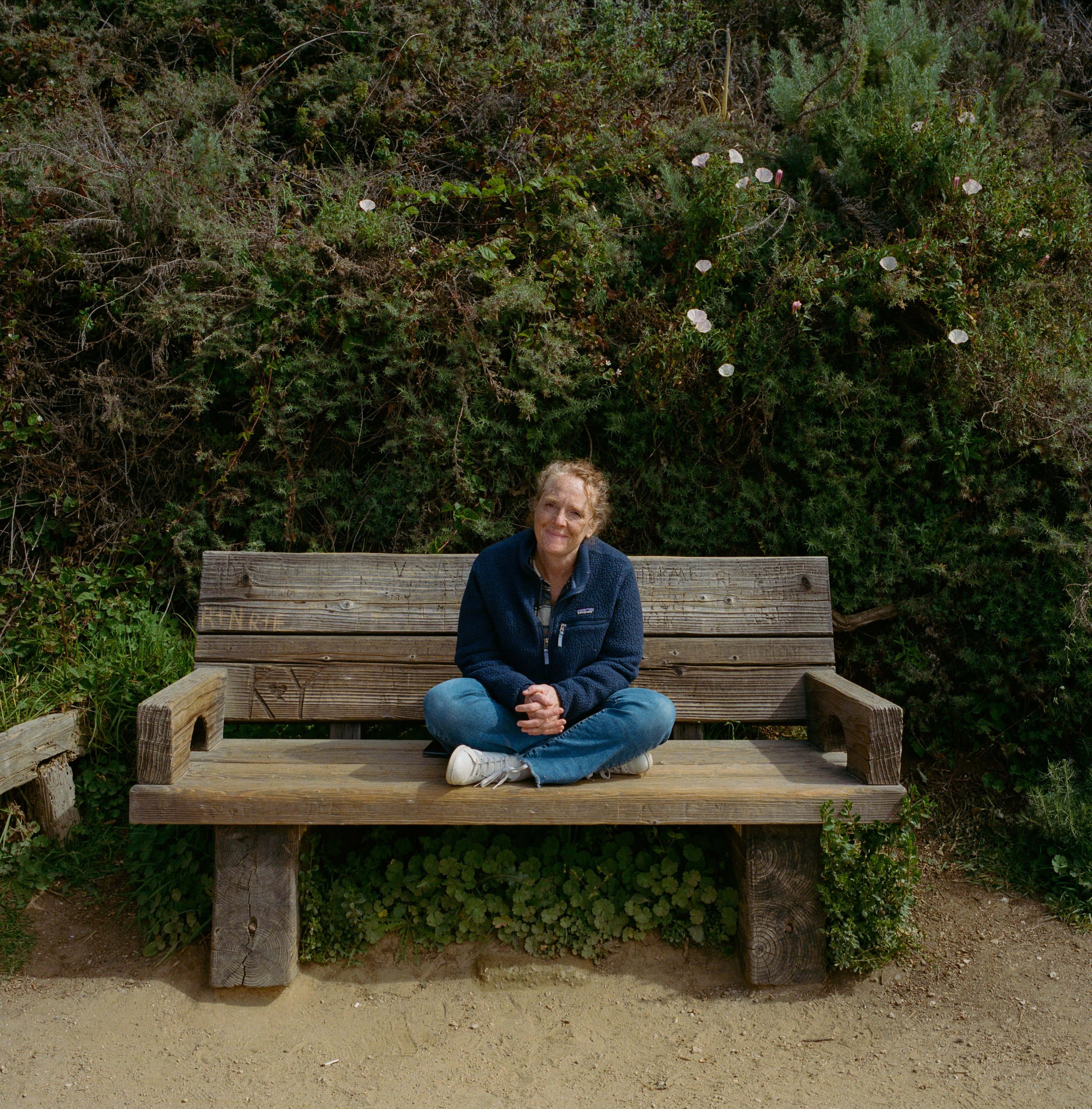 Malaurie Hotier sitting cross-legged on a wooden bench outdoors