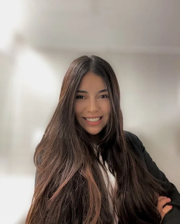 A woman with long dark brown hair smiling and wearing a black blazer.