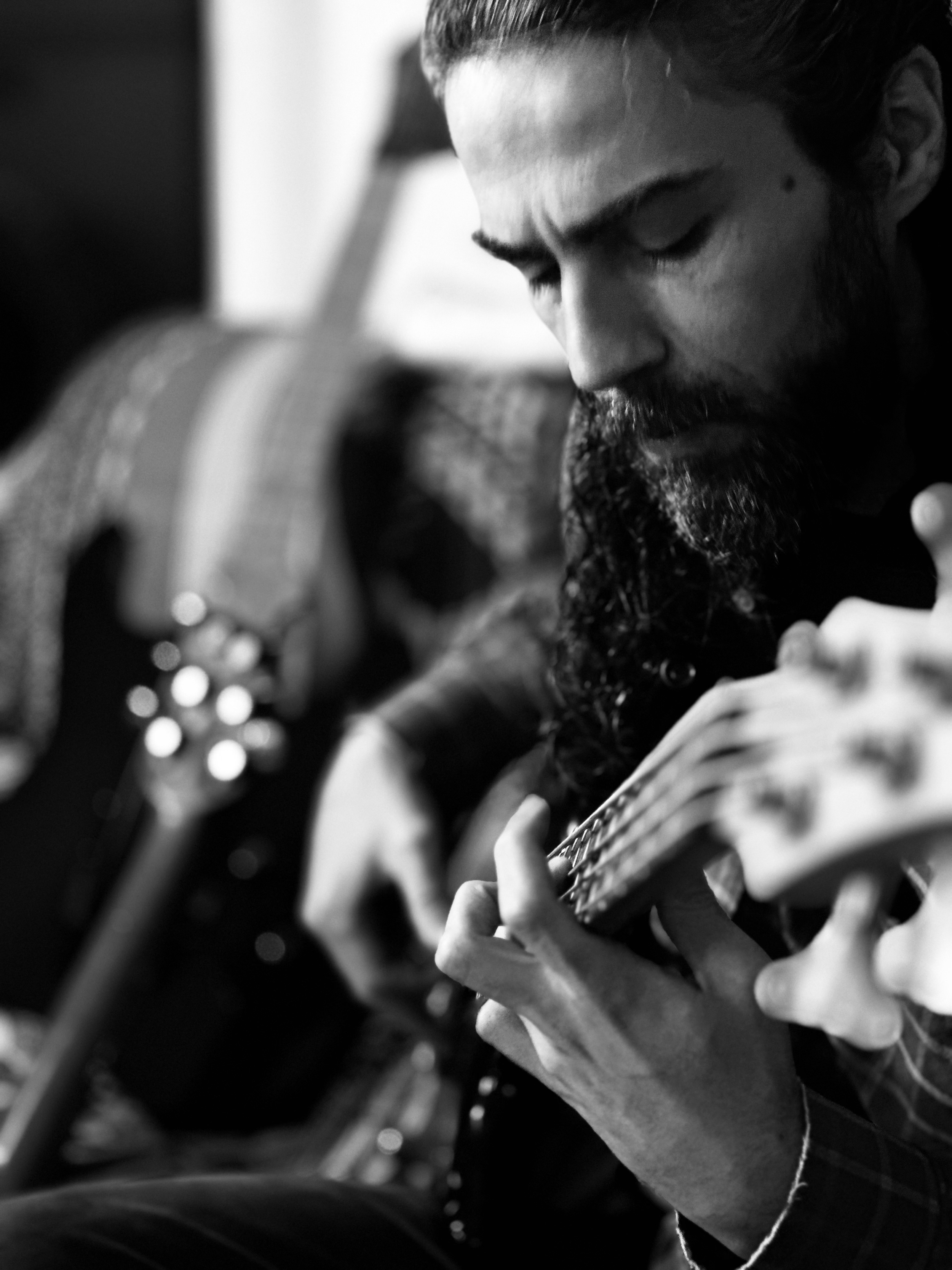Homem tocando guitarra em preto e branco, focado na música. Close das mãos nas cordas e expressão concentrada.