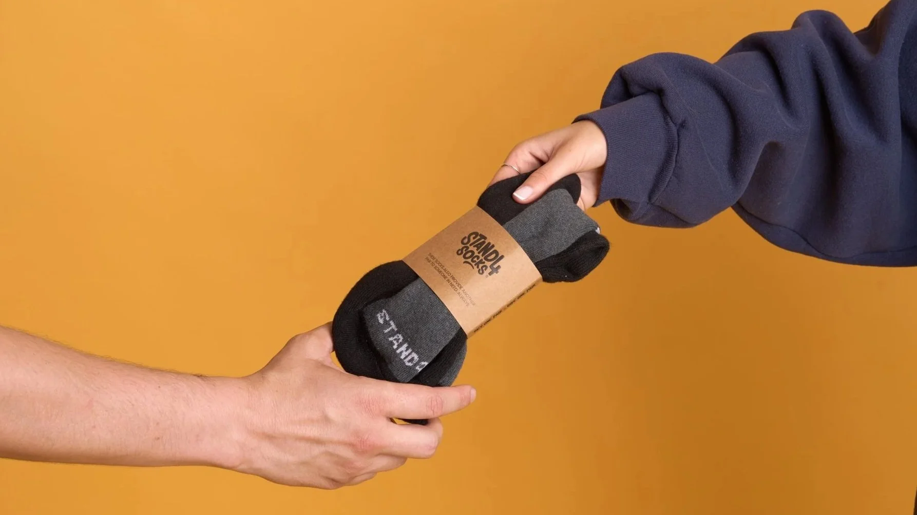 Close-up of one person handing a bundled pair of black Stand4 donation socks to another