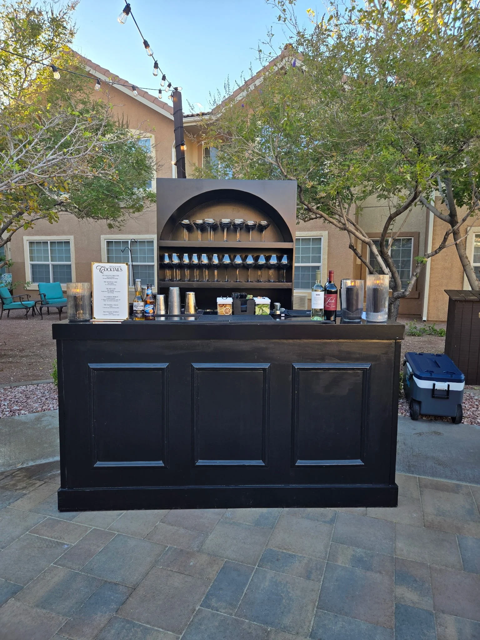 Three colorful cocktails with fruit garnishes and mint leaves on a table with scattered fruit slices and leaves, with a person standing behind.