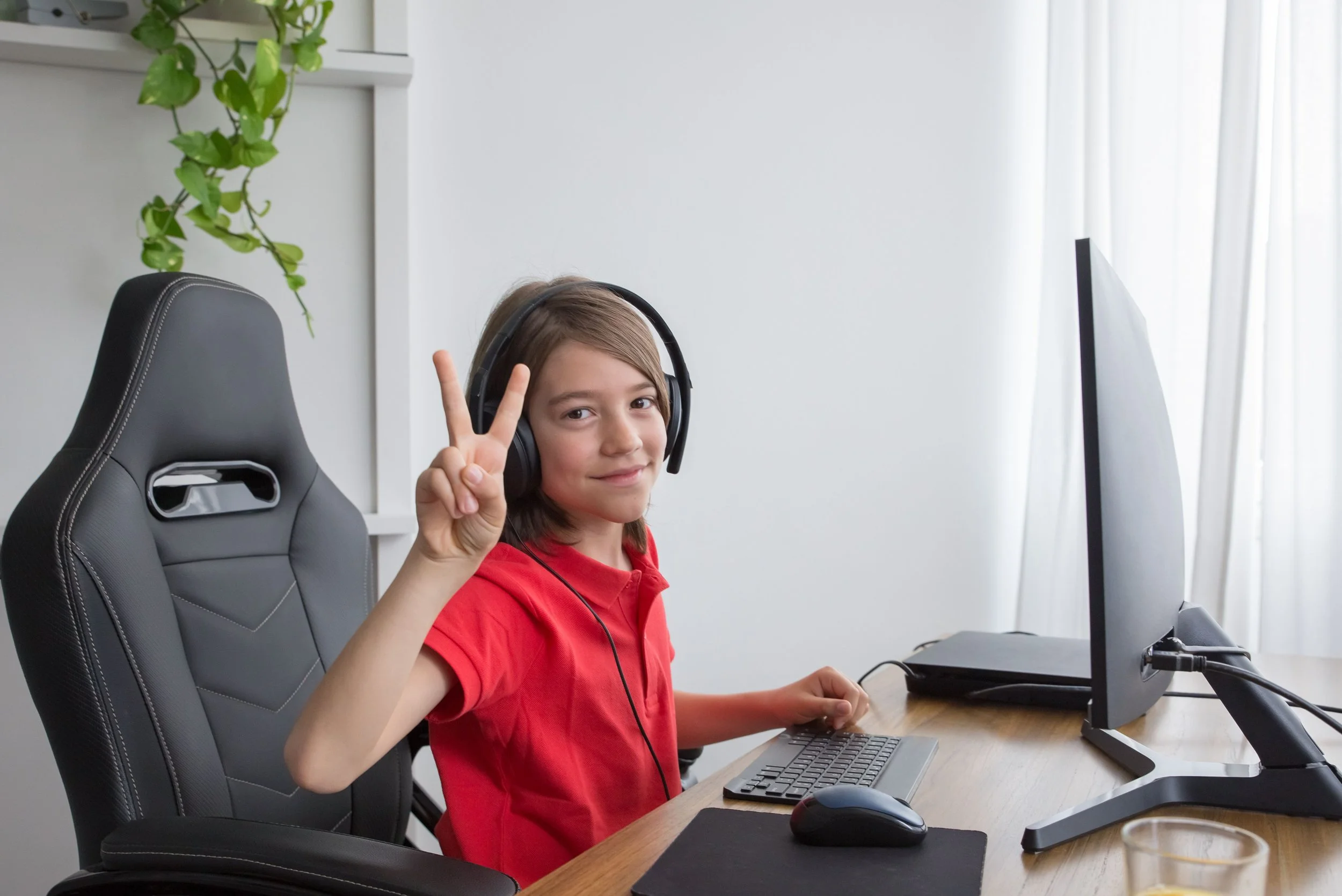 A virtual student sits at a desk and holds up a peace sign