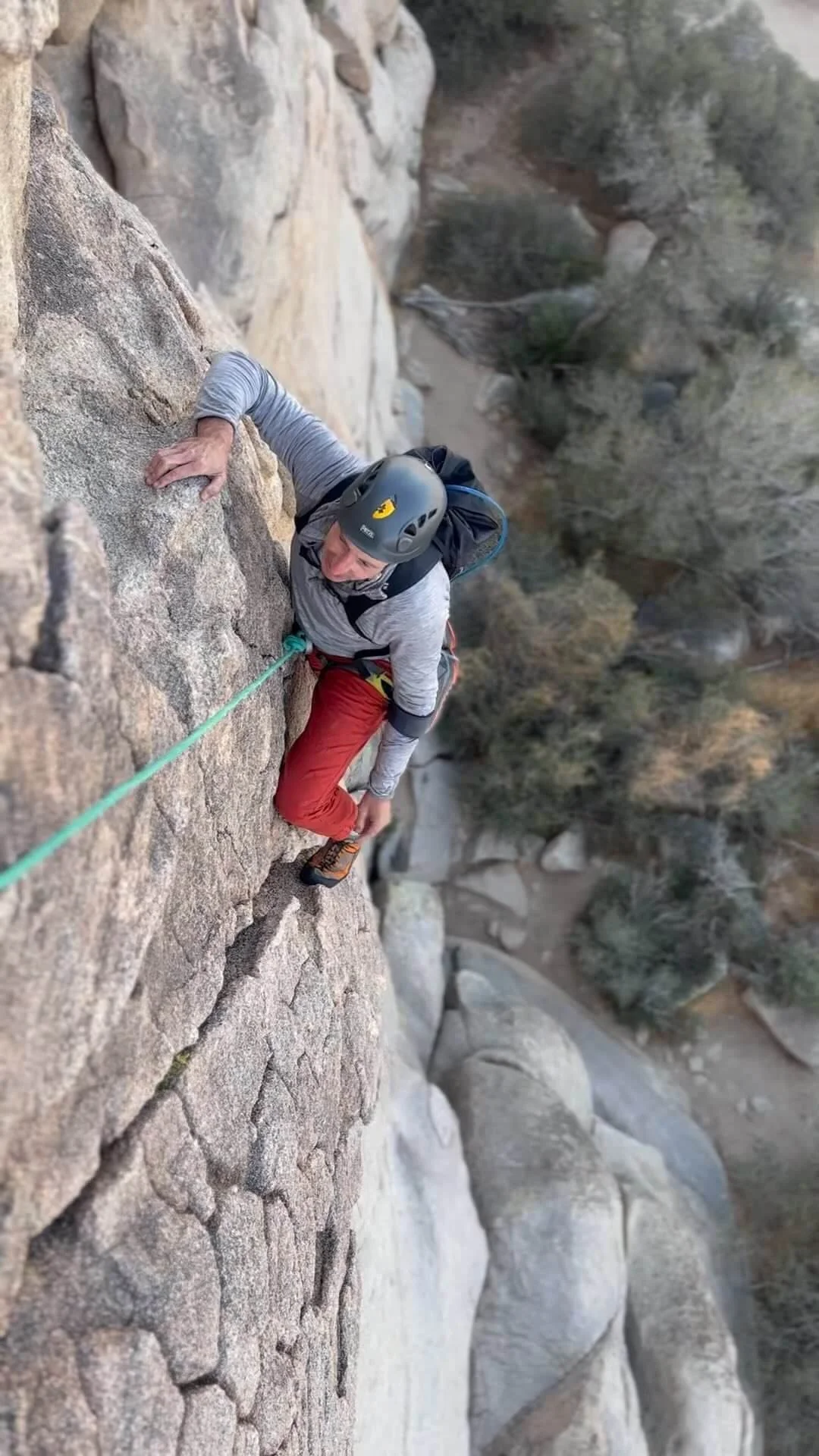 A man rock climbing on a steep outdoor cliff with a green safety rope.