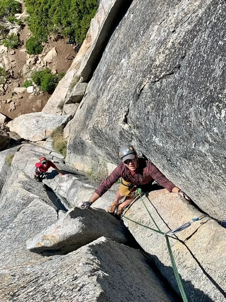 A woman rock climbing on a steep cliff face with a mountain landscape in the background.