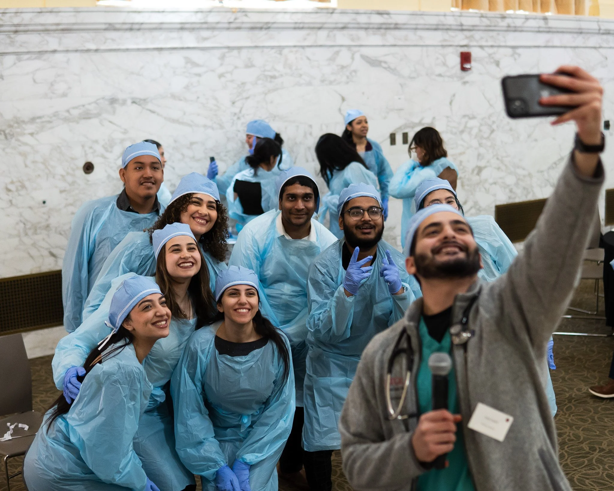 Group of people in medical uniforms taking a selfie in an indoor setting with a marble wall in the background.