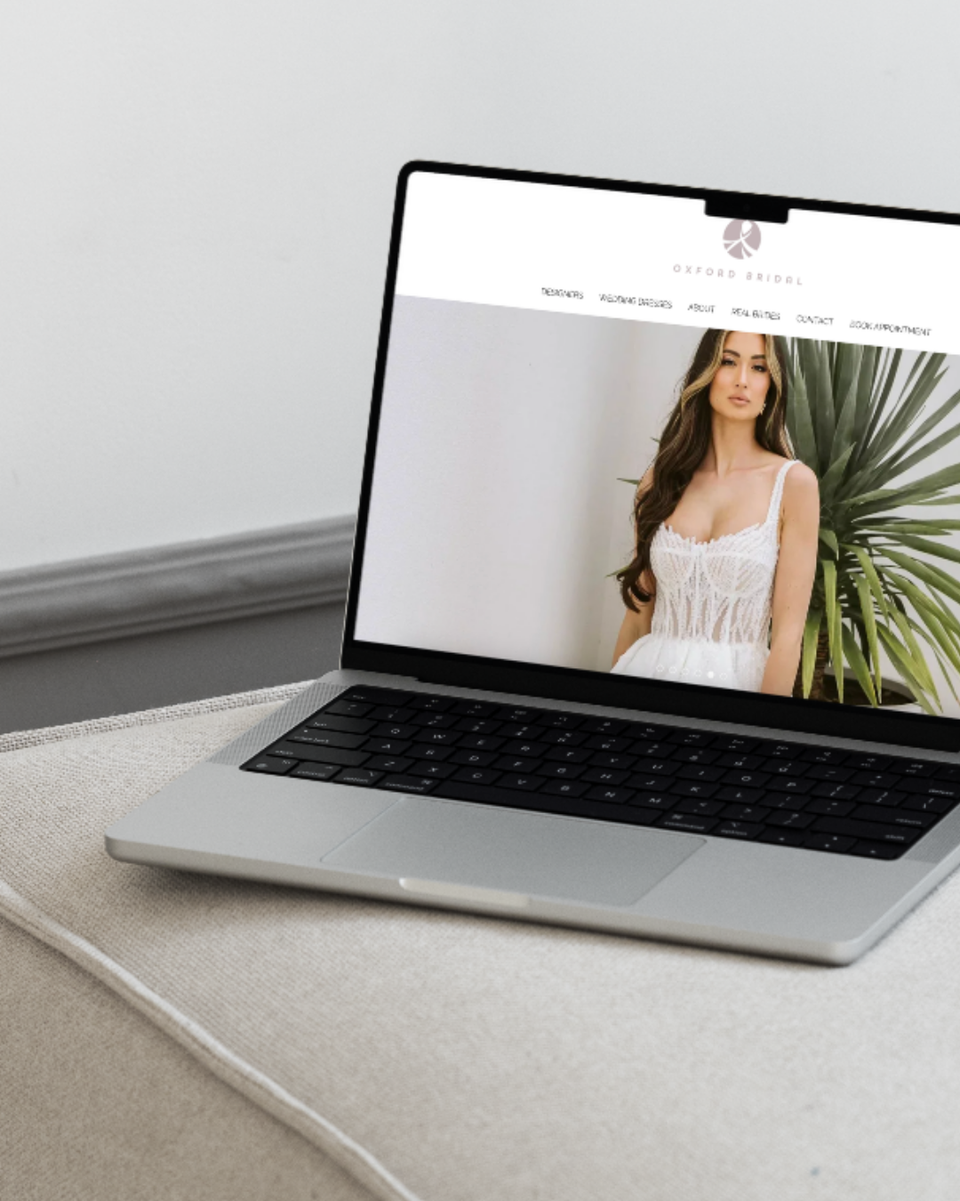 Open laptop displaying a webpage for Oxford Bridal with a photo of a woman in a white dress standing next to a large green plant.