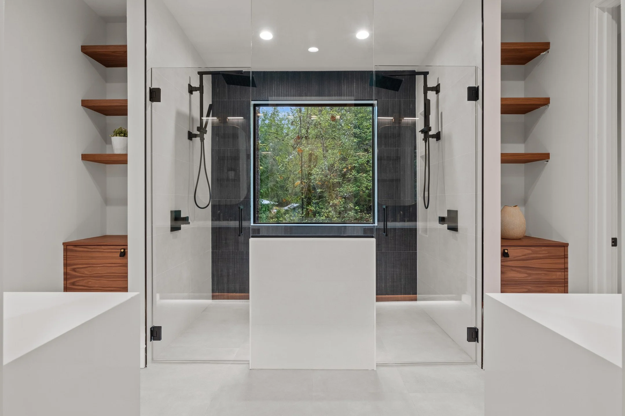 View into this amazing spa-like bathroom in H2D Architecture + Design's recently completed new custom home in Issaquah. This primary bathroom is designed with a curb-less walk in shower with double shower heads and view to the forest beyond. Open and