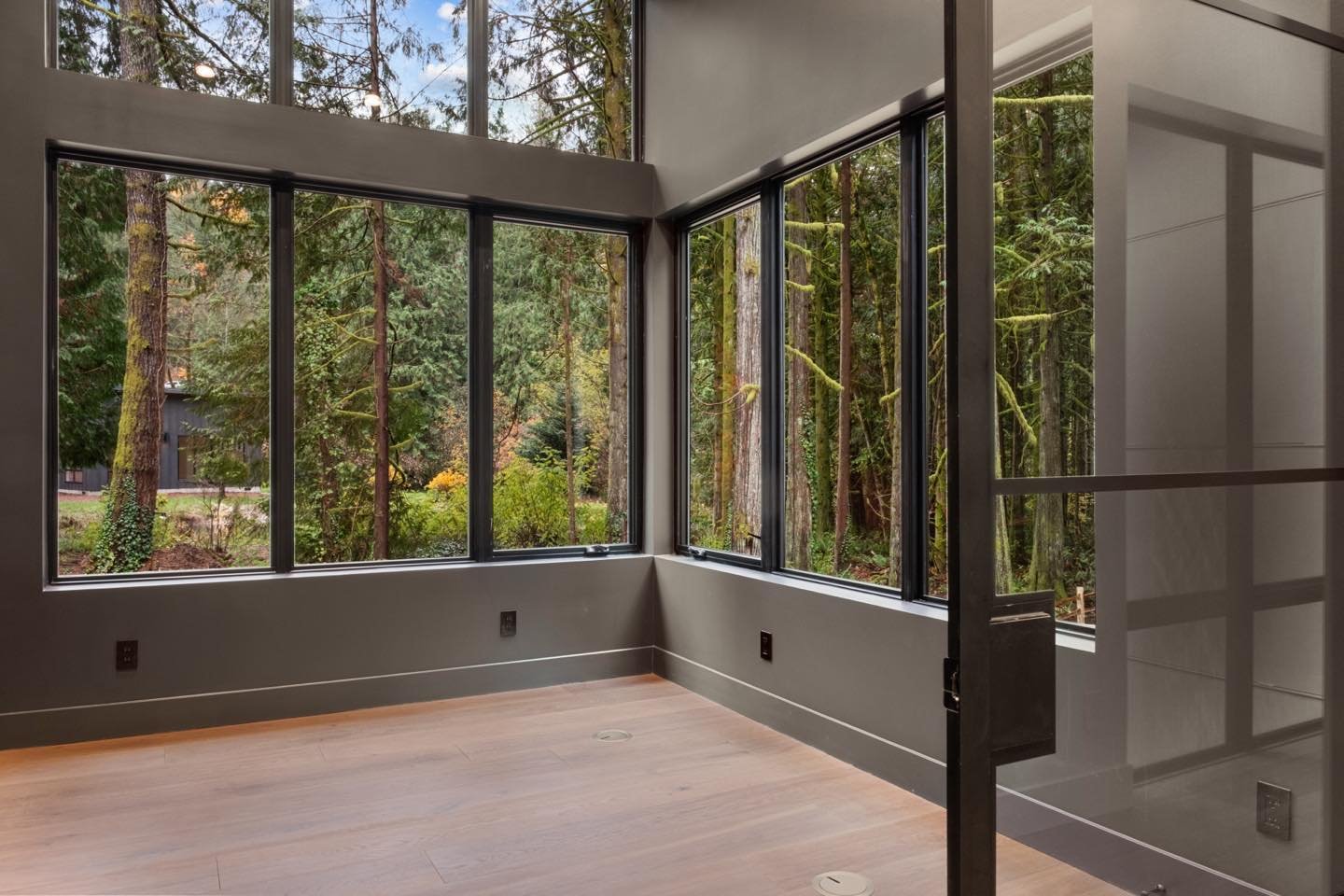 Two walls of windows in this home office provide territorial views into the private wooded lot in this recently completed new custom home in Issaquah by H2D Architecture + Design.  This home office is separated from the main hallway with a glass slid