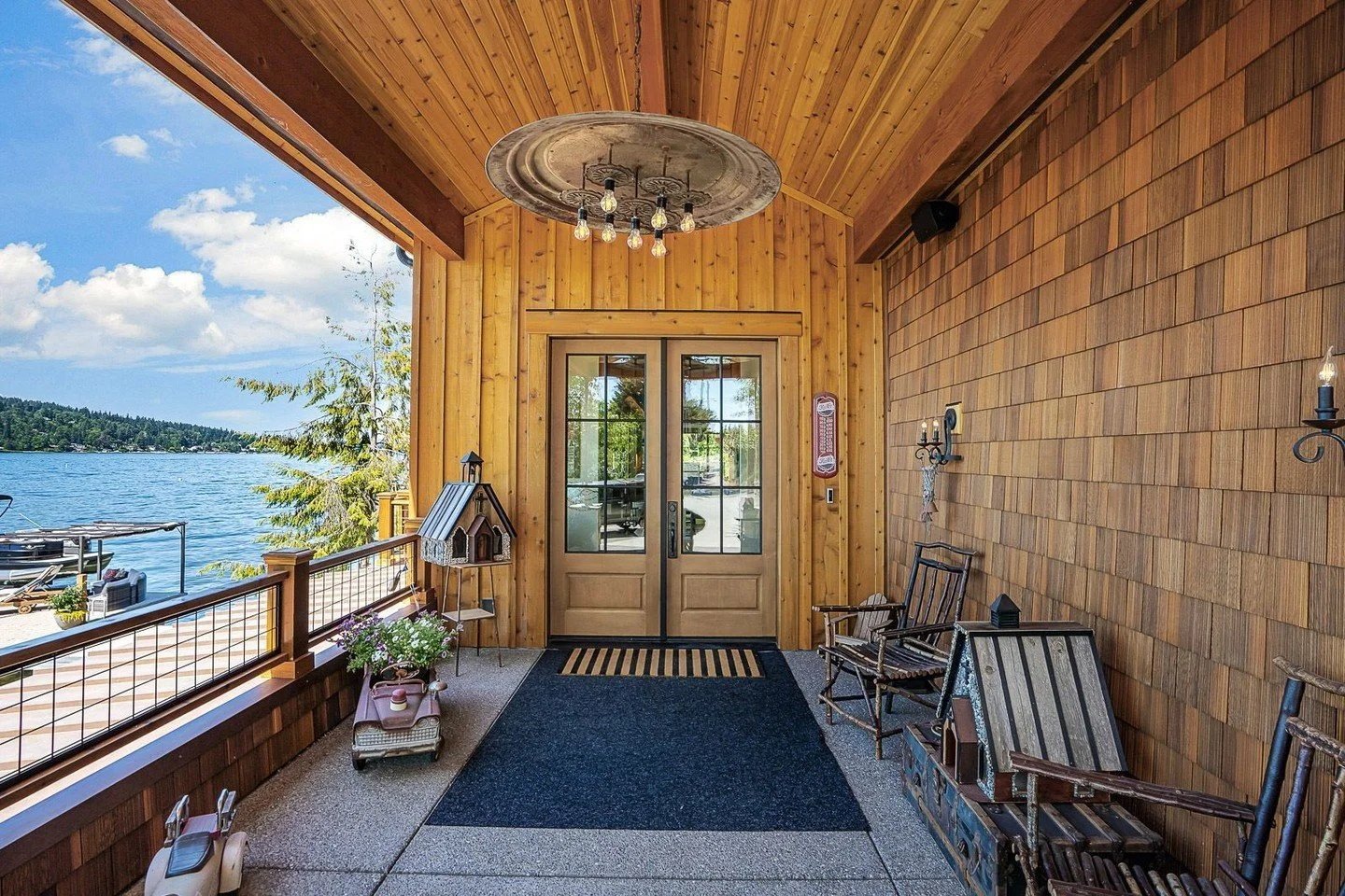 The entry of this new custom Lake Washington home by H2D Architecture + Design welcomes guests with a generous covered area and view of the lake. Its rustic character is captured with an aged metal chandelier and warm wood textures that wrap the wall