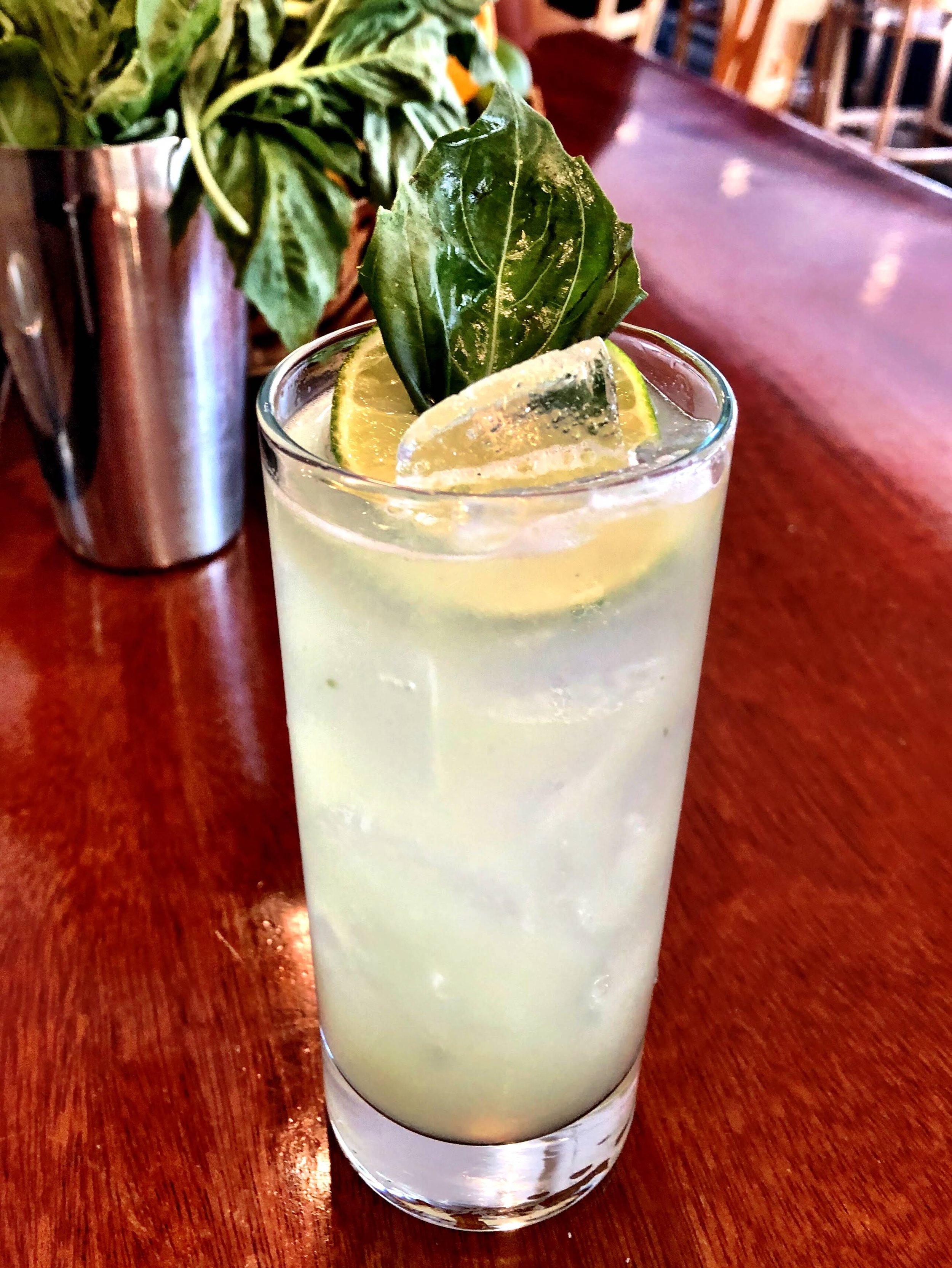 Refreshing cocktail with ice and basil garnish on a wooden table