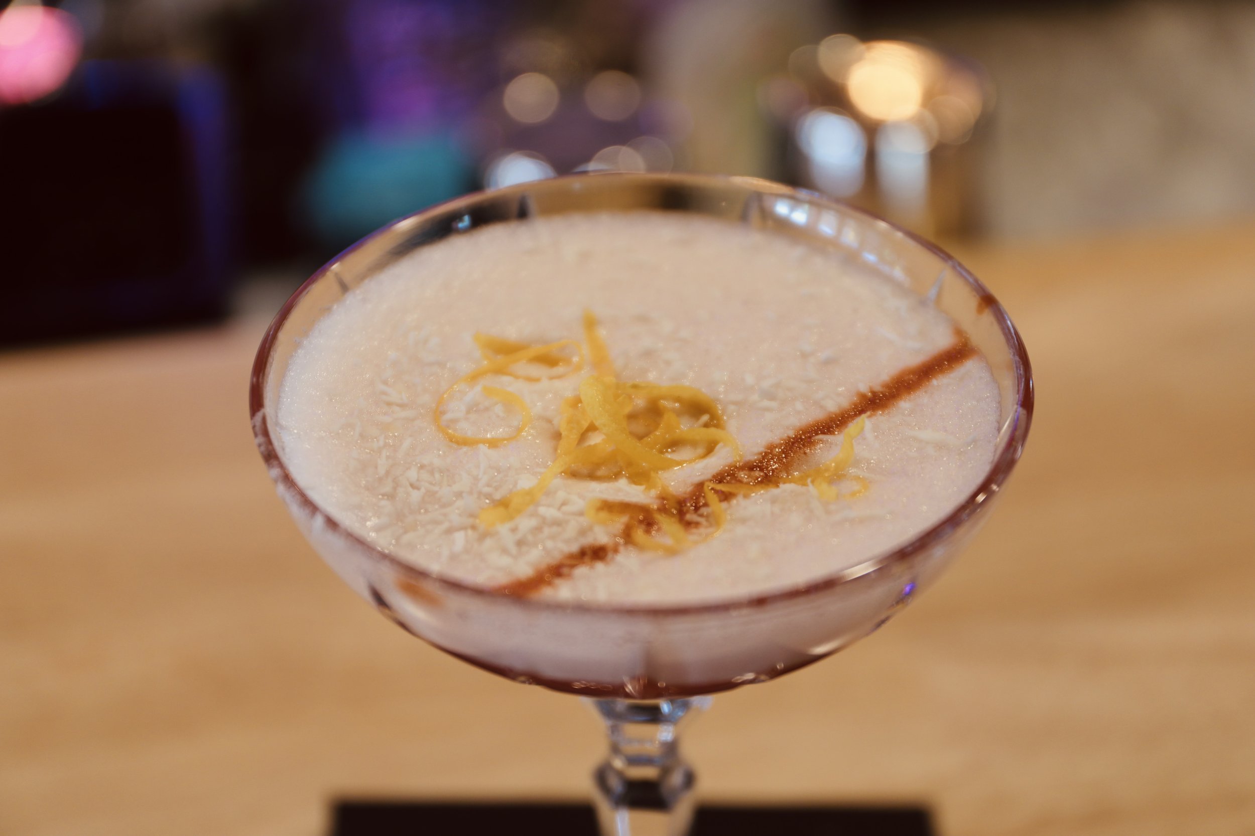 Cocktail in a glass with lemon zest and coconut flakes on top