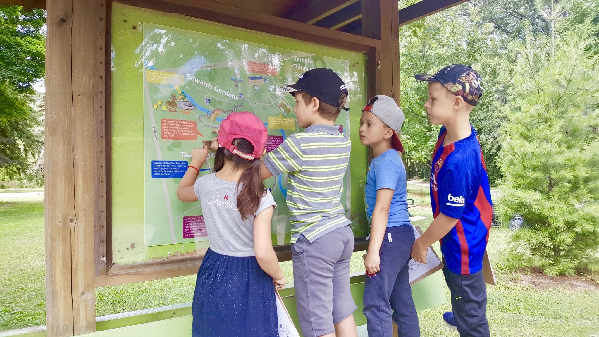 Children looking at a map on a wooden board outdoors.