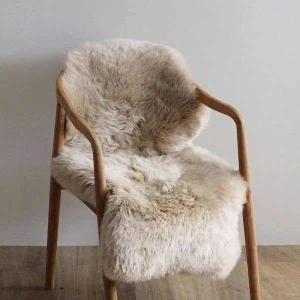 A wooden chair with a fluffy fibre sheepskin coat draped over it, placed against a plain wall.