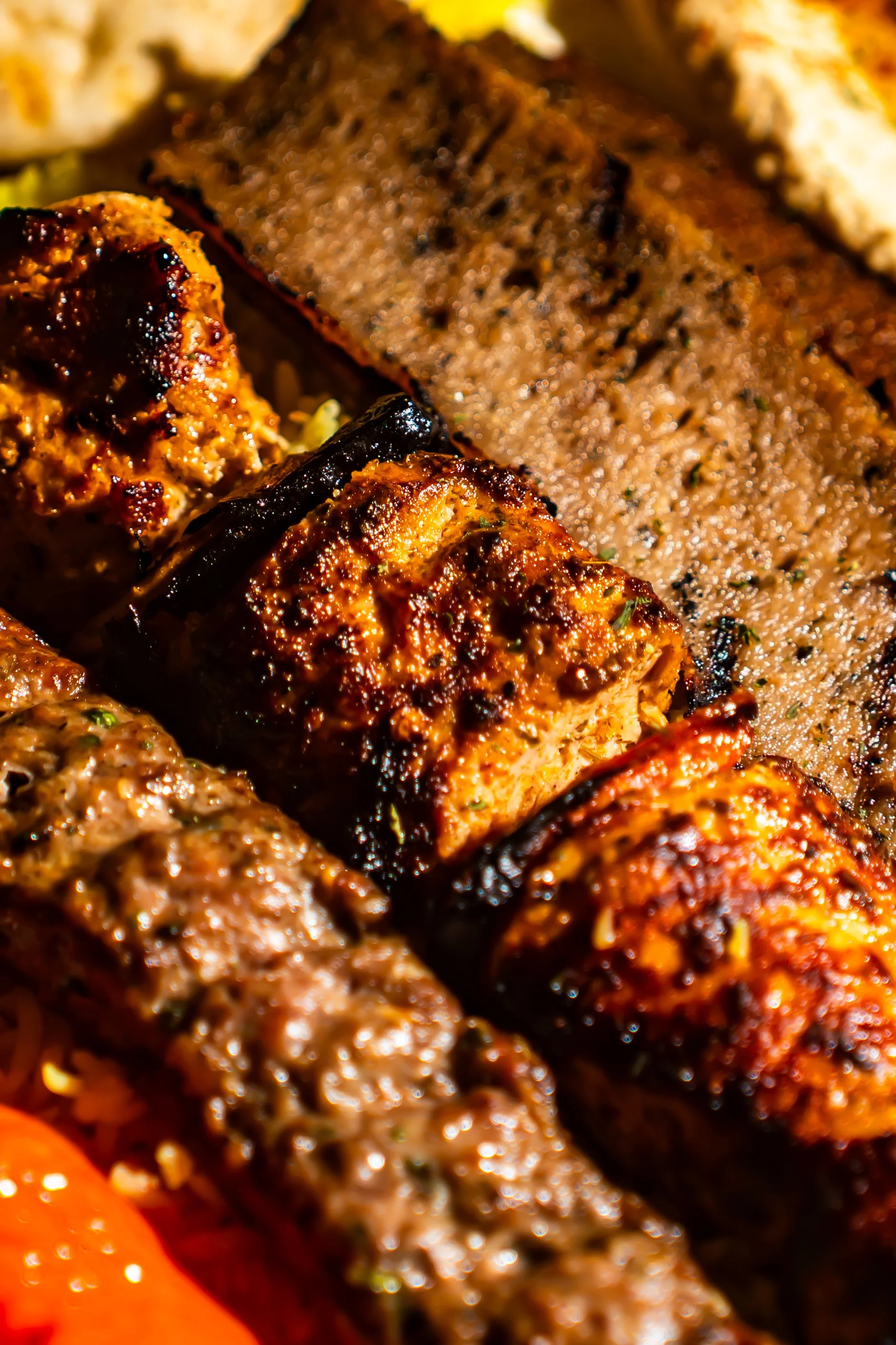 Close-up of various grilled meat kebabs, including beef and possibly chicken or lamb, with a grilled beef patty and a beef steak in the background.