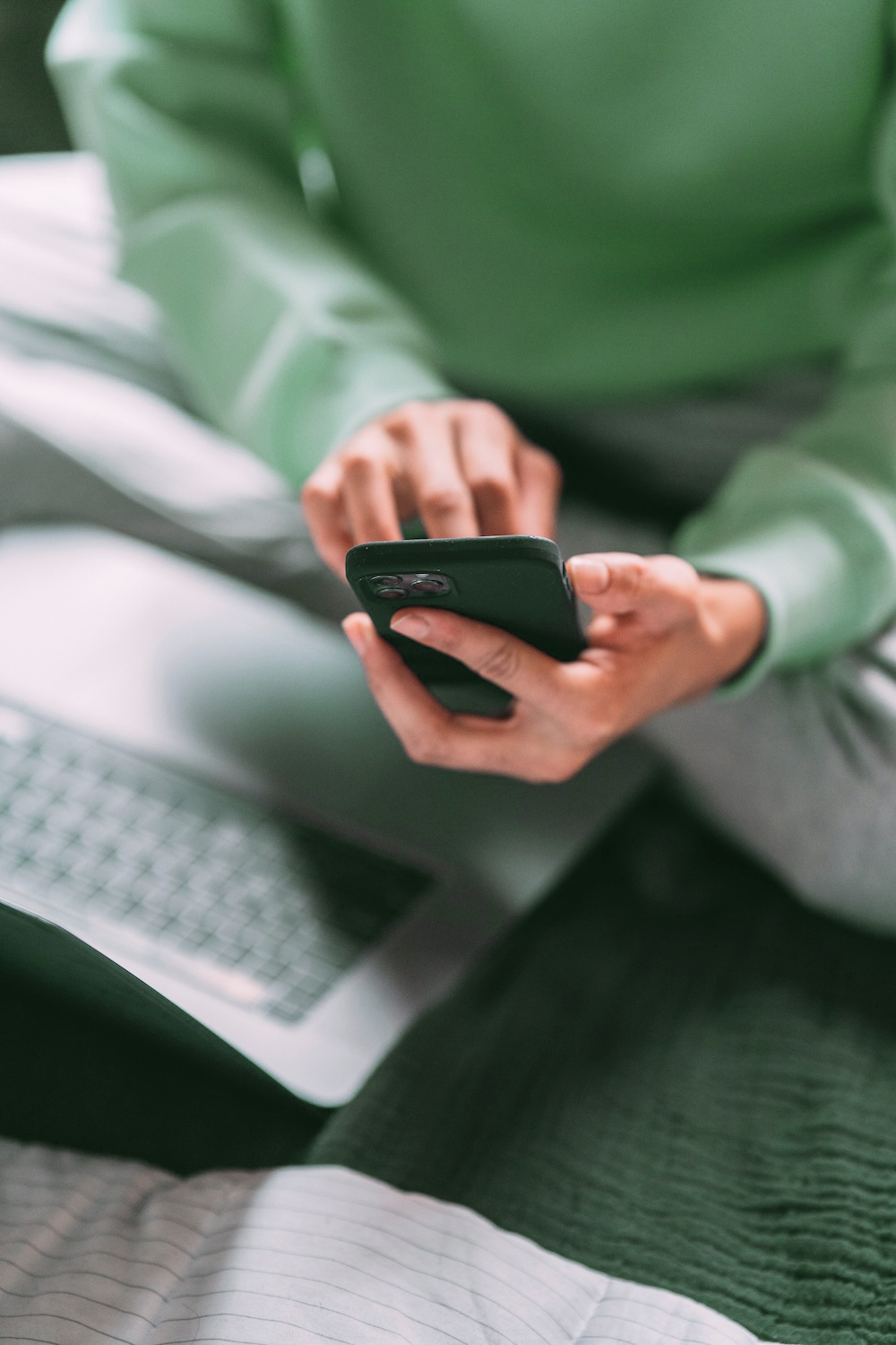 Person holding a phone over a laptop and typing something on it. They have pale skin and short nails.