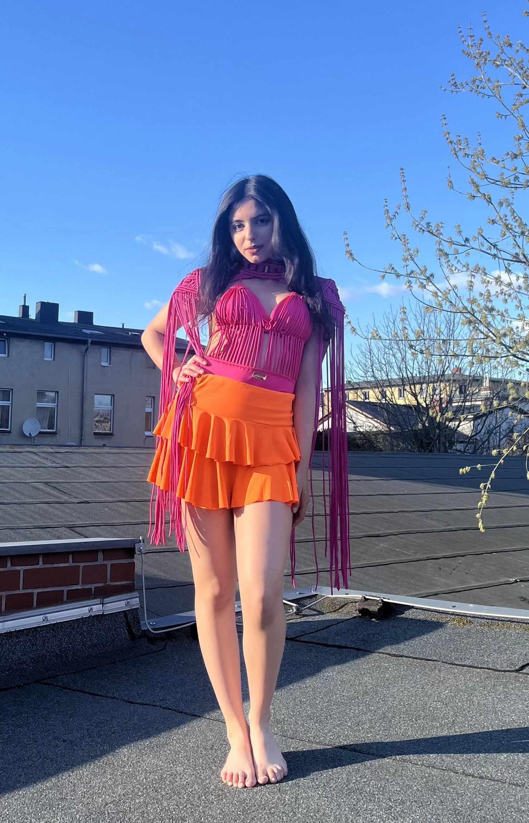 Junge Frau in buntem Kleid ohne Schuhe auf einem Dach bei Sonnenuntergang