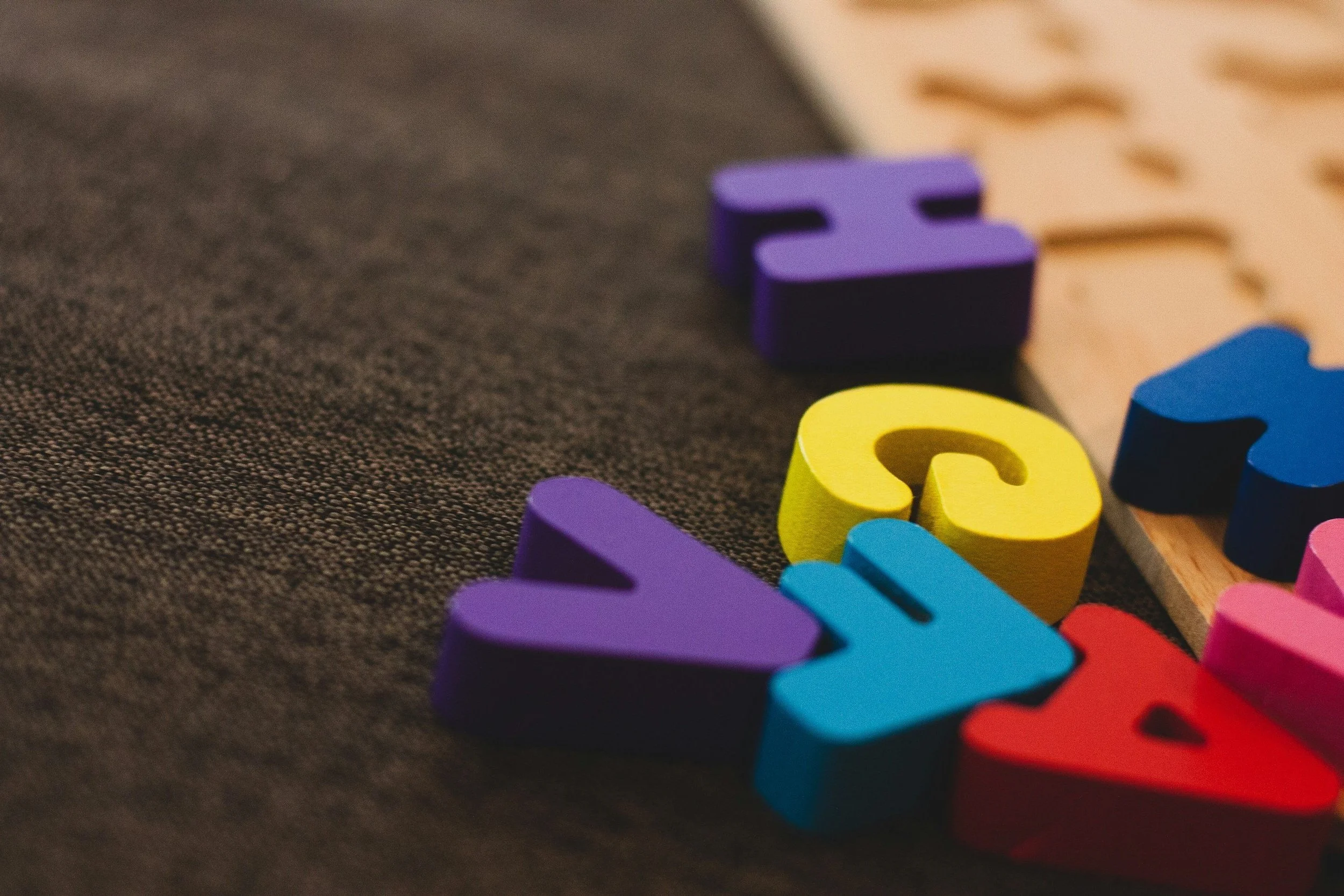 Colorful foam blocks with various shapes and letters placed on a textured dark fabric surface and a wooden board.