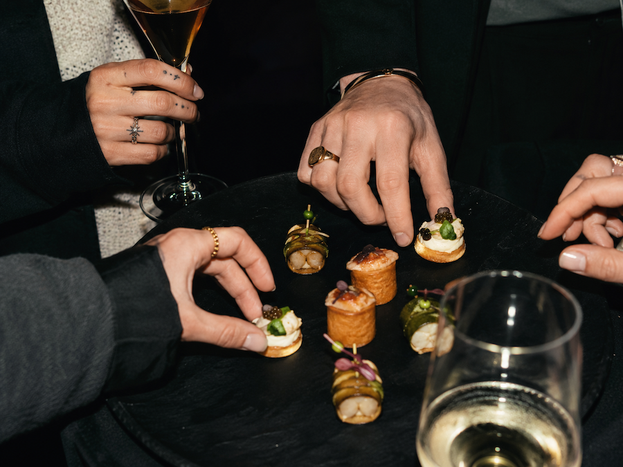 Personen beim Gabeln von kleinen Canapés und Sekt im Glas