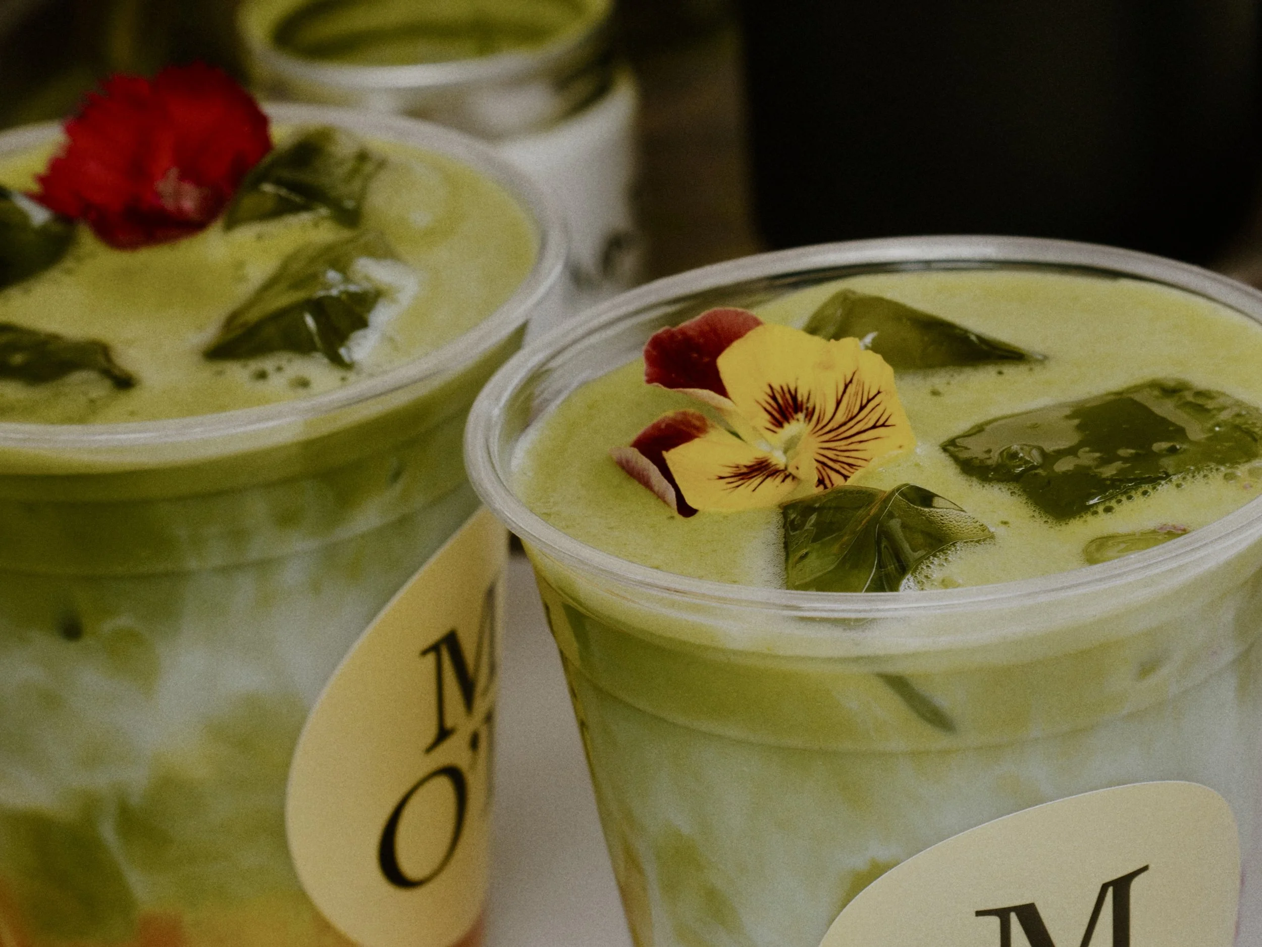 Zwei grüne Pudding- oder Smoothie-Becher, verziert mit essbaren Blüten und Blättern.