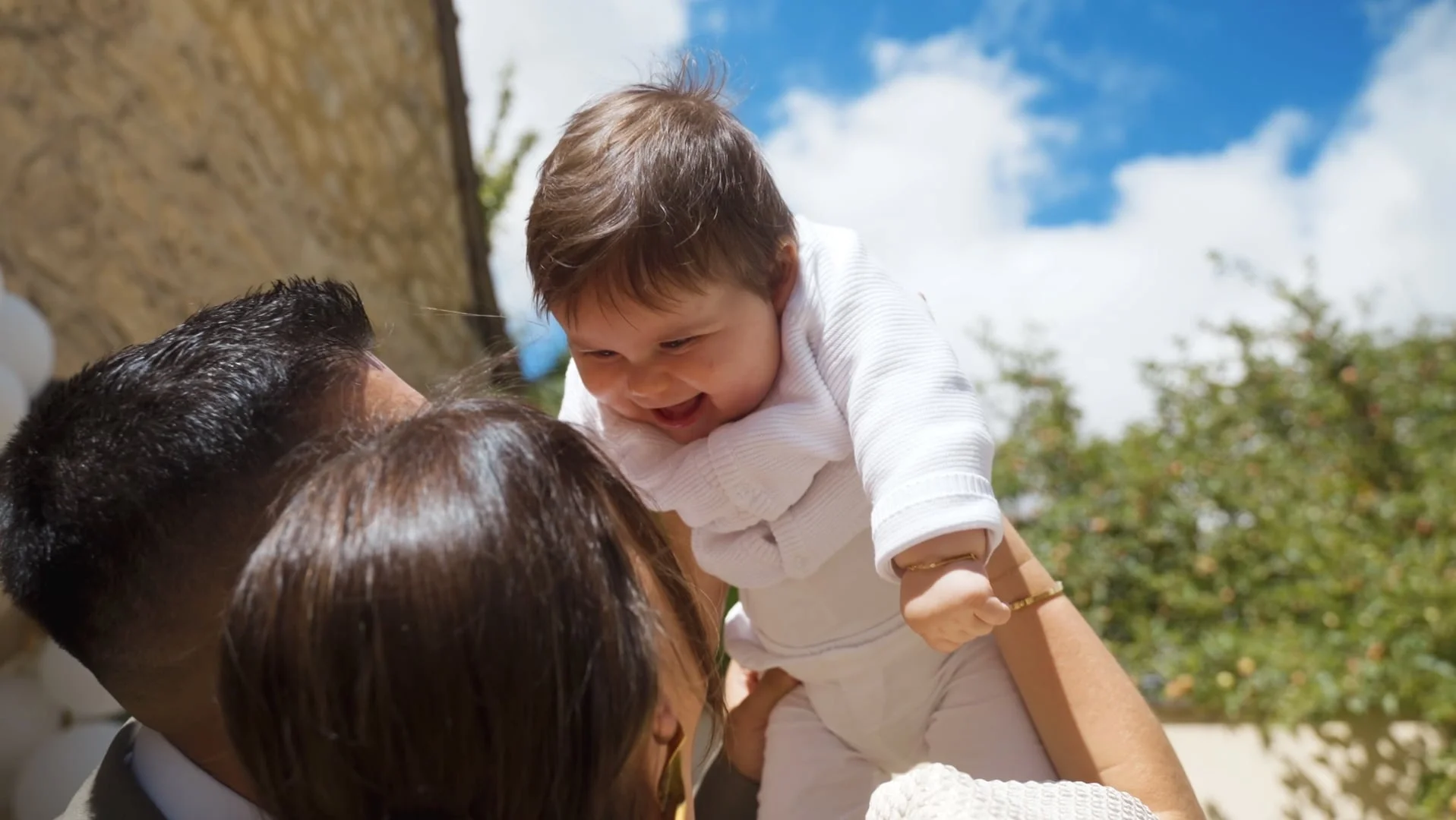 Bébé porté en l'air par ses parents lors de son baptême.