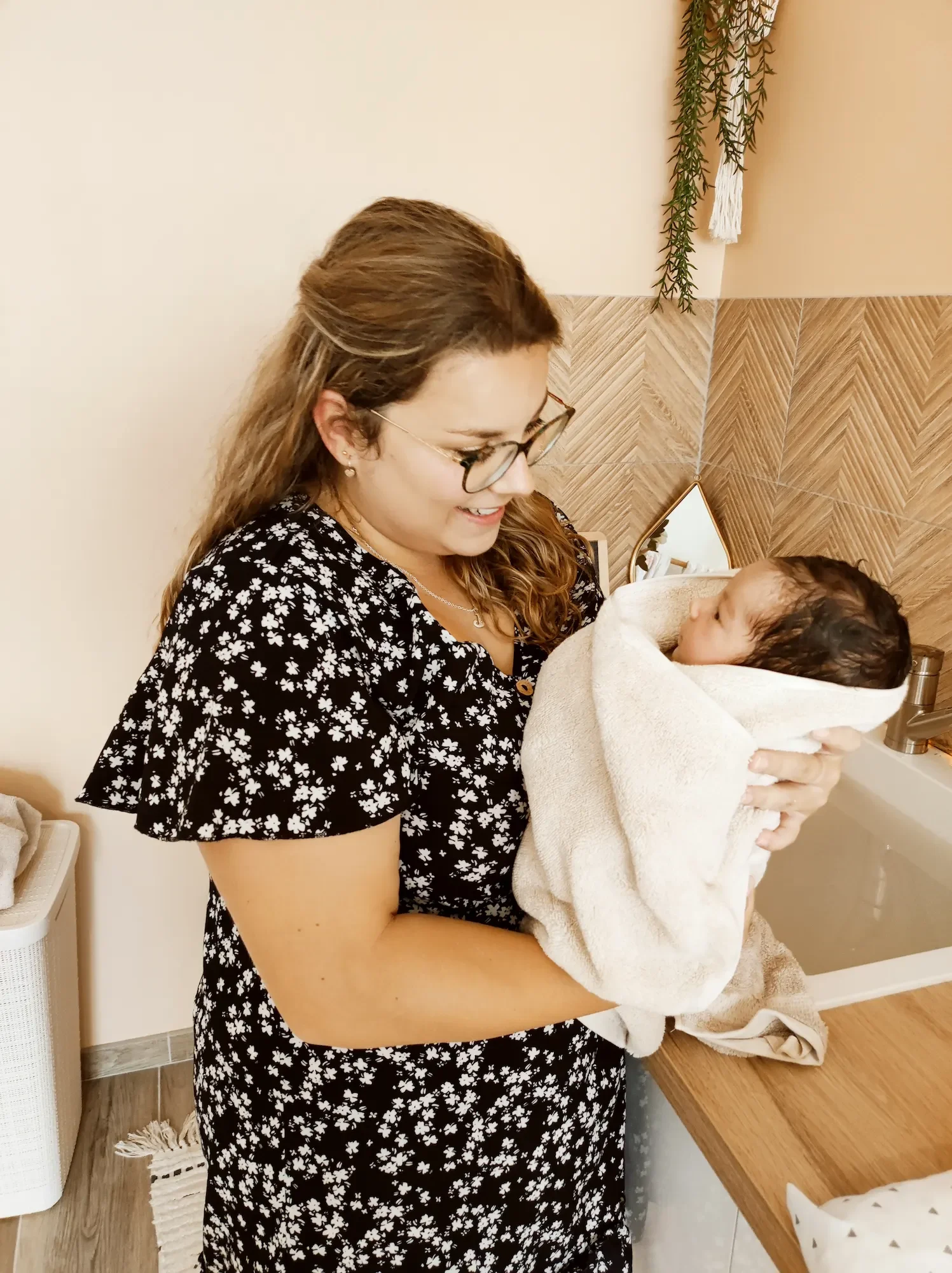 Portrait de Juliette Lepetit qui est auxiliaire de puériculture et qui porte un bébé enveloppé dans une serviette après un bain thérapeutique.
