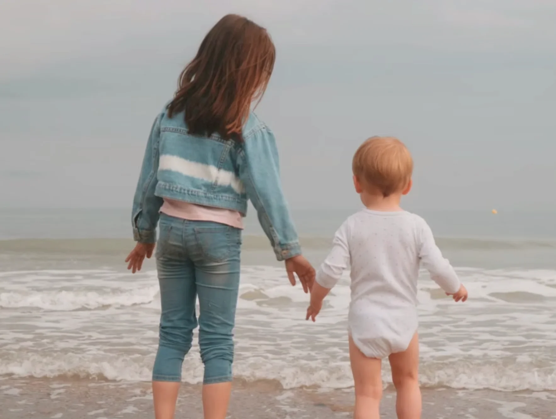 Séance famille en vidéo à la plage de Merville-Franceville en Normandie où on voit une petite fille de dos avec son petit-frère.