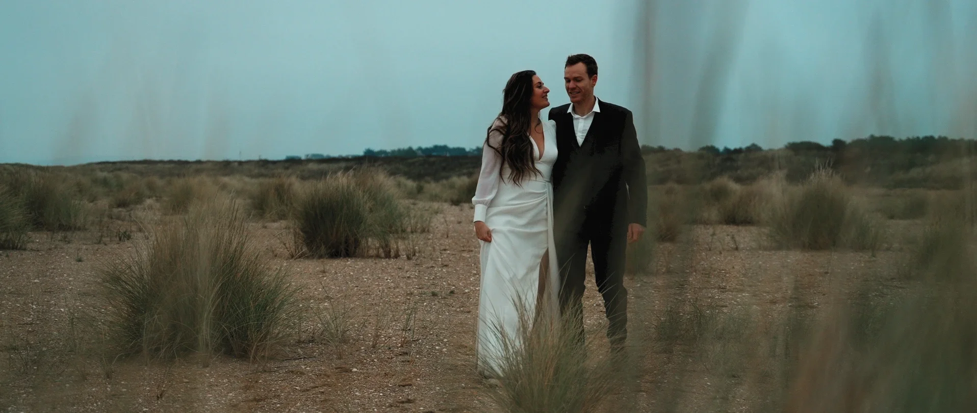 Séance trash the dress d'Anaïs et Étienne à la plage de Merville-Franceville en hiver après leur mariage. On les voit marcher de face en se tenant.