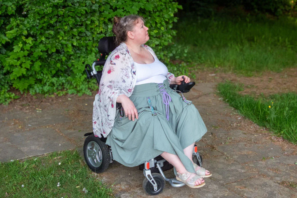 A woman in a wheelchair is wearing a skirt with hikes keeping the hem from catching in the wheels of the wheelchair