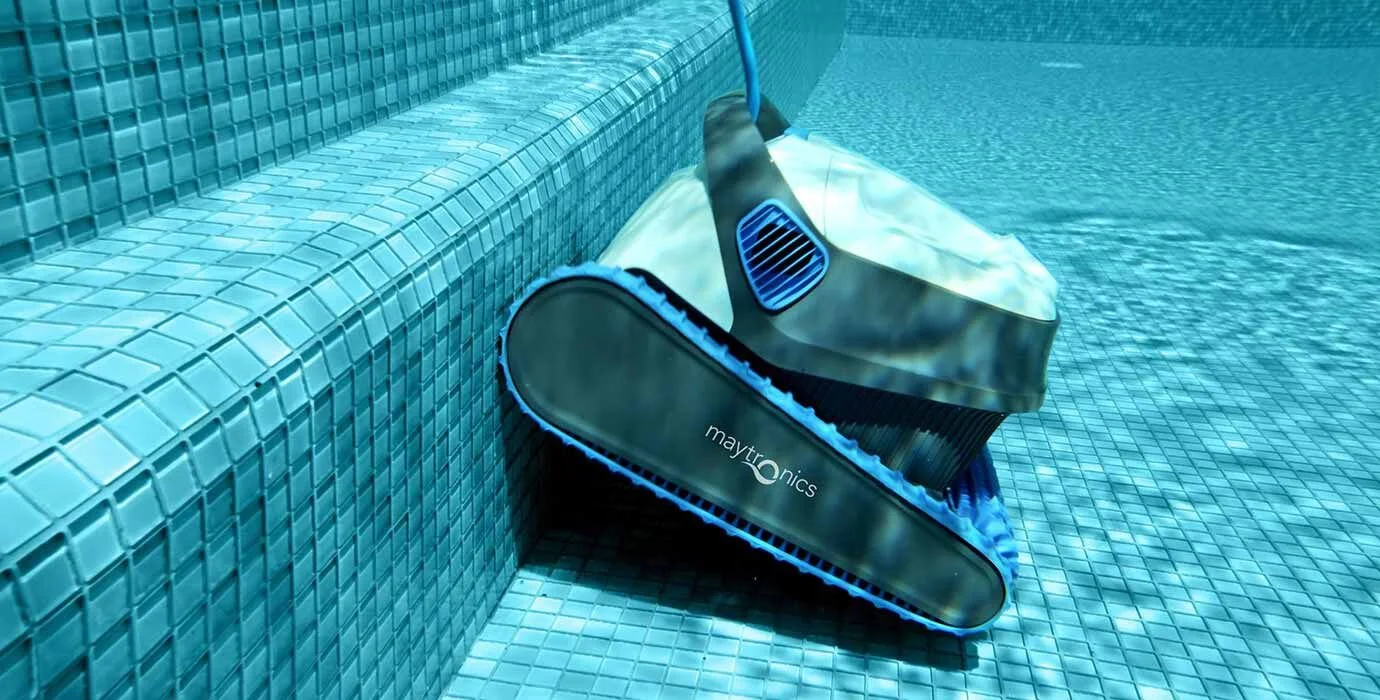 Robot nettoyeur de piscine sous l'eau, Maytronics, sur un fond de carreaux de piscine bleus.