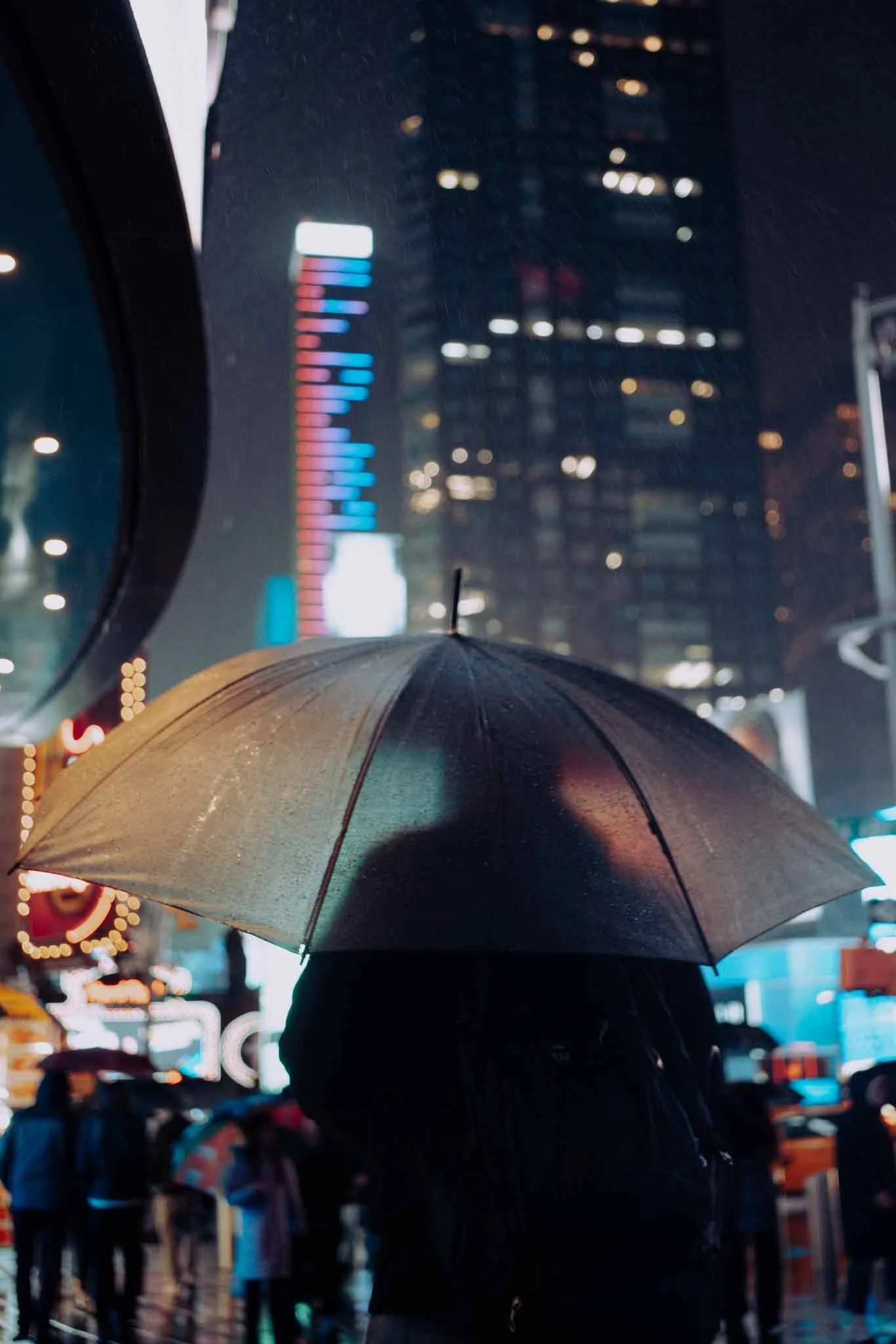 A man holds his umbrella close as he passes through Times Square in New York City on a rainy night.