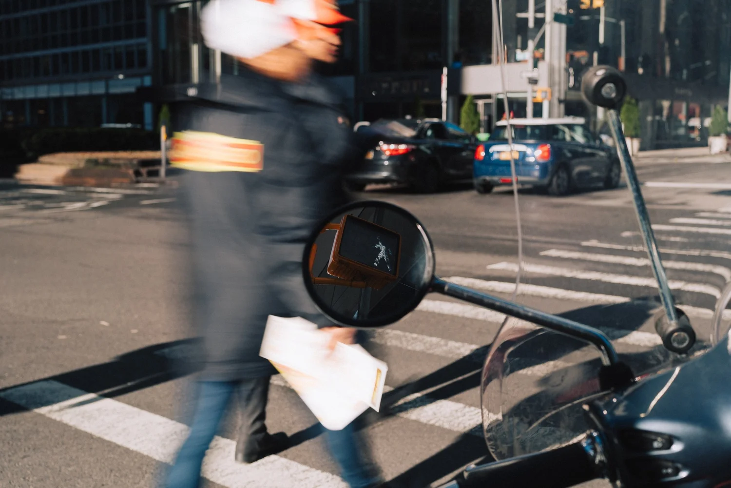 Scooter mirror reflecting a walk signal as a blurred man passes