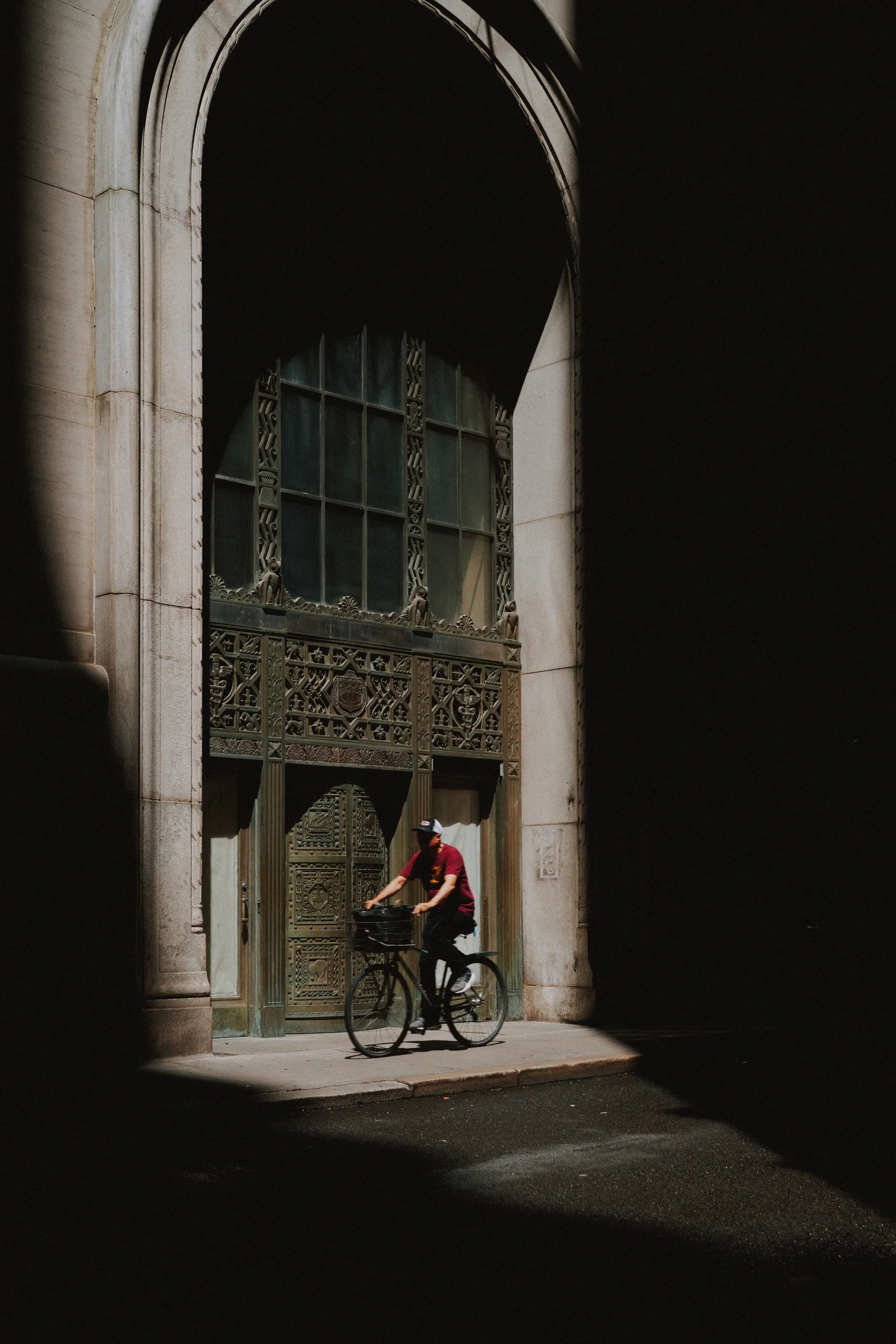 Cyclist passing an ornate bronze doorway inside a shadowed stone arch
