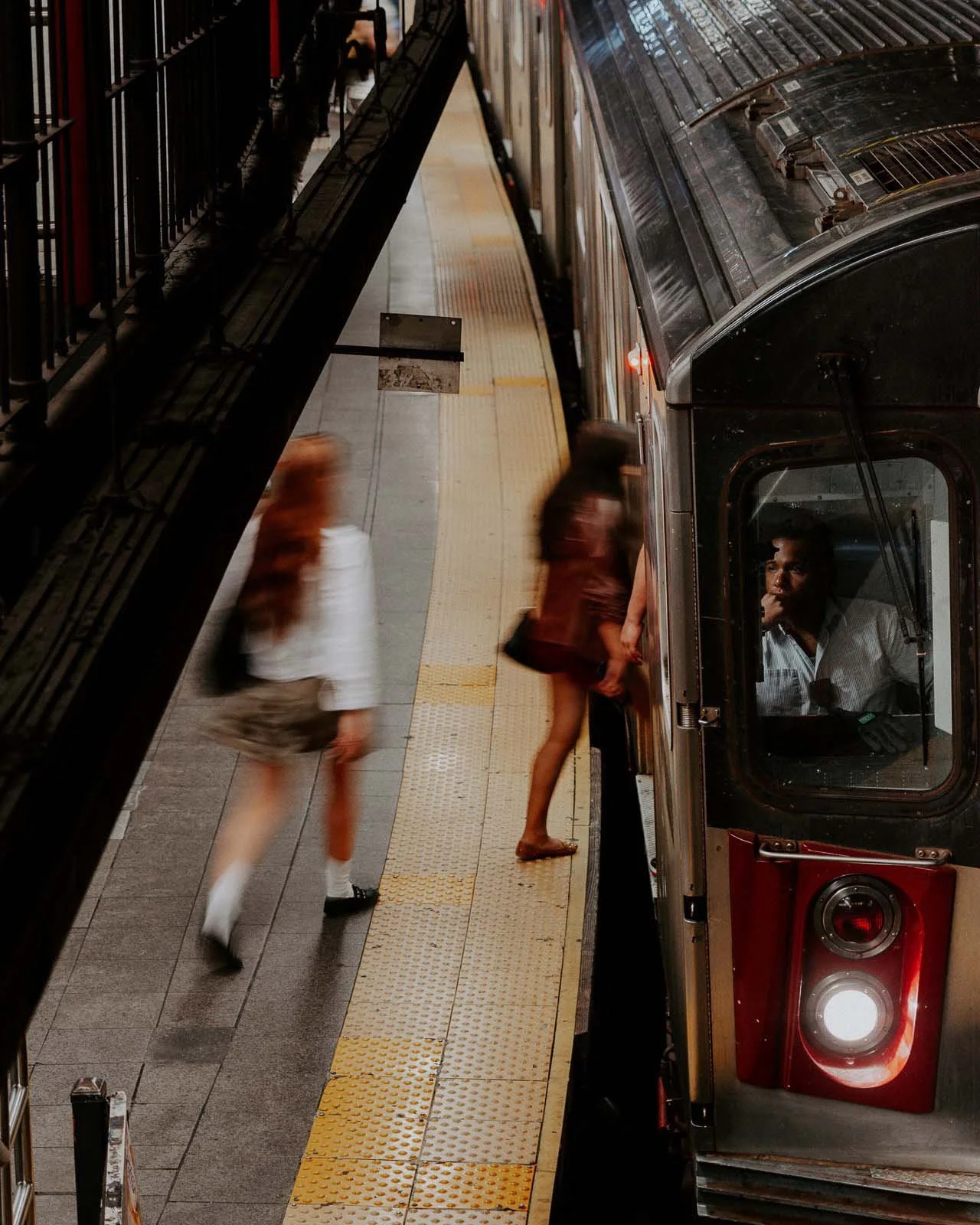A train operator is depicted gazing longingly out of the window as people enter the train, capturing a moment of introspection and reflection.