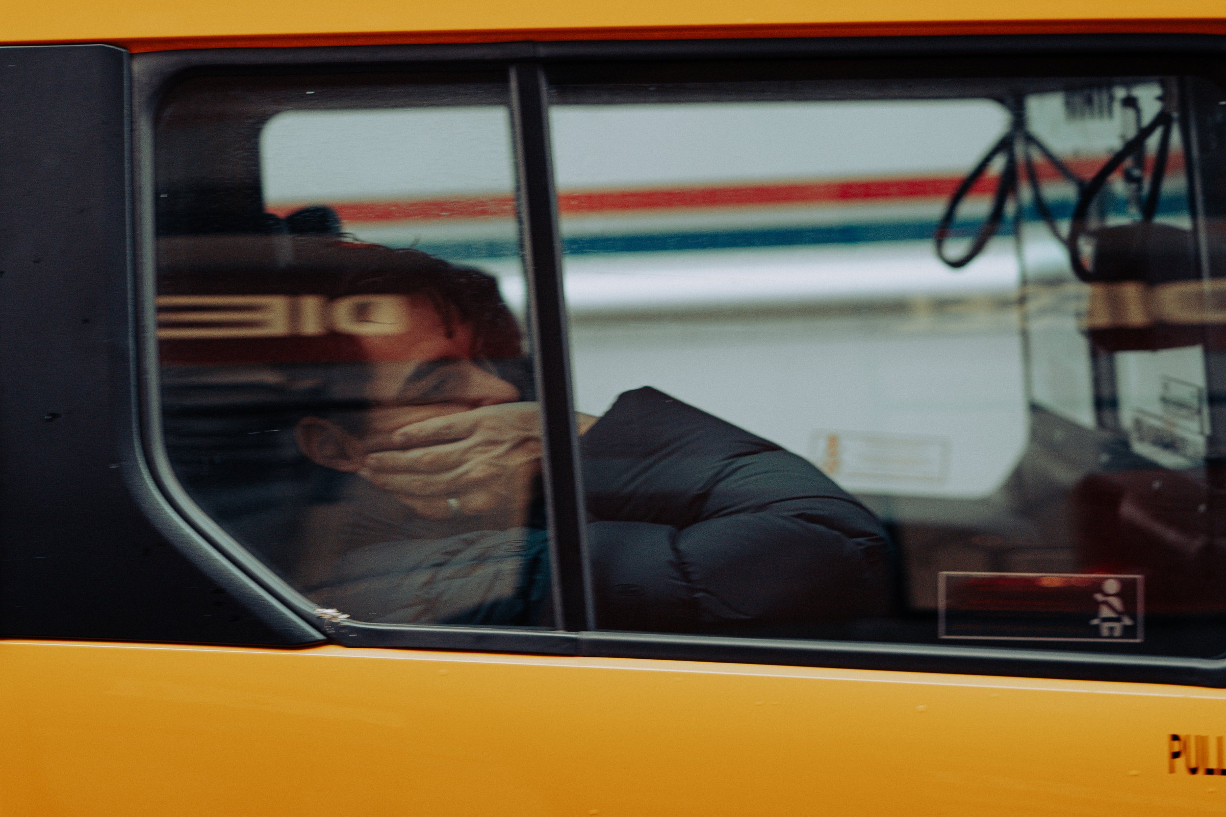 Reflection of a person seen through the window of a yellow taxi cab with the word 'DIE' reversed on the reflection