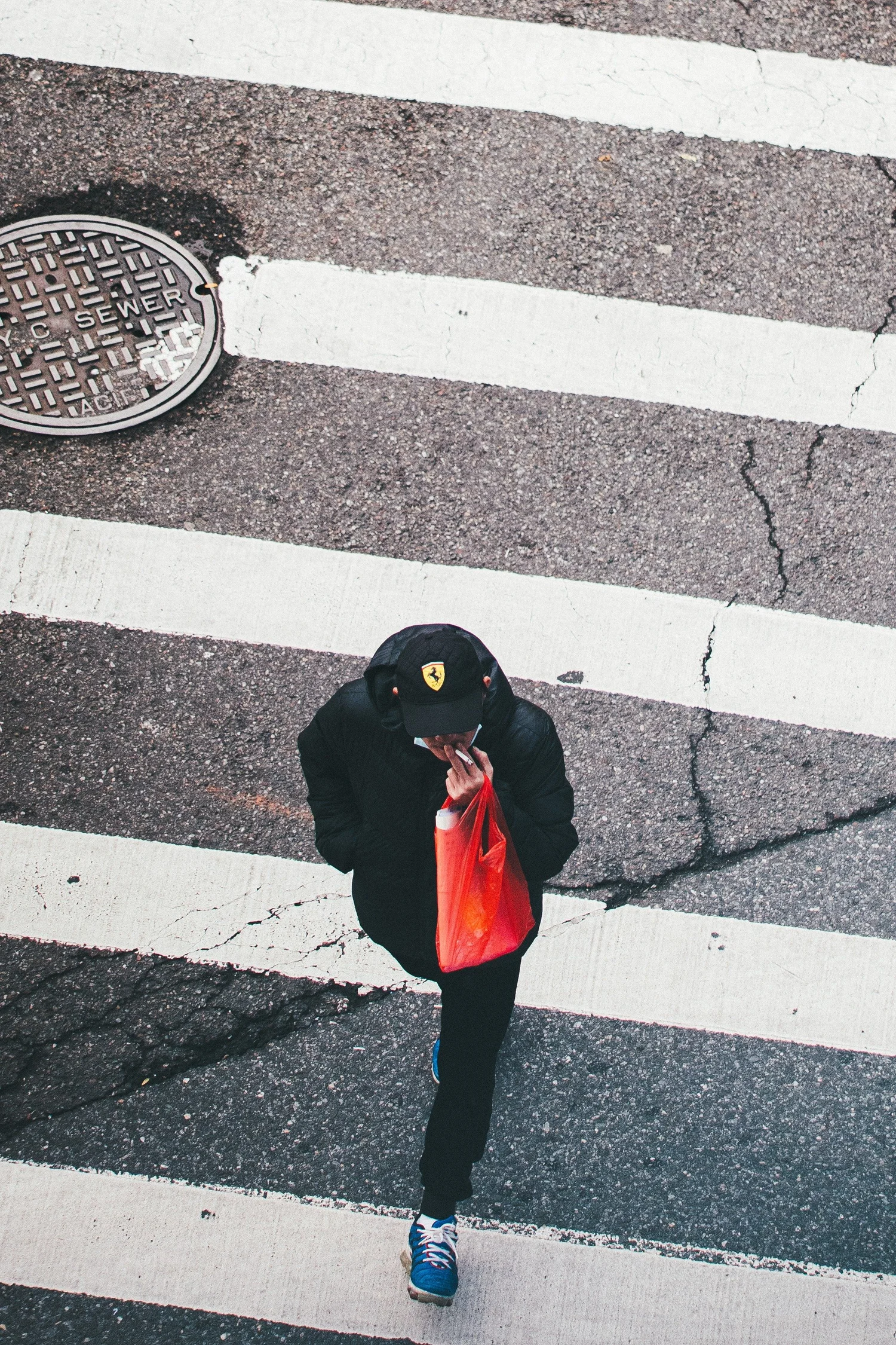 Overhead view of a man in a Ferrari cap with a red bag crossing a crosswalk