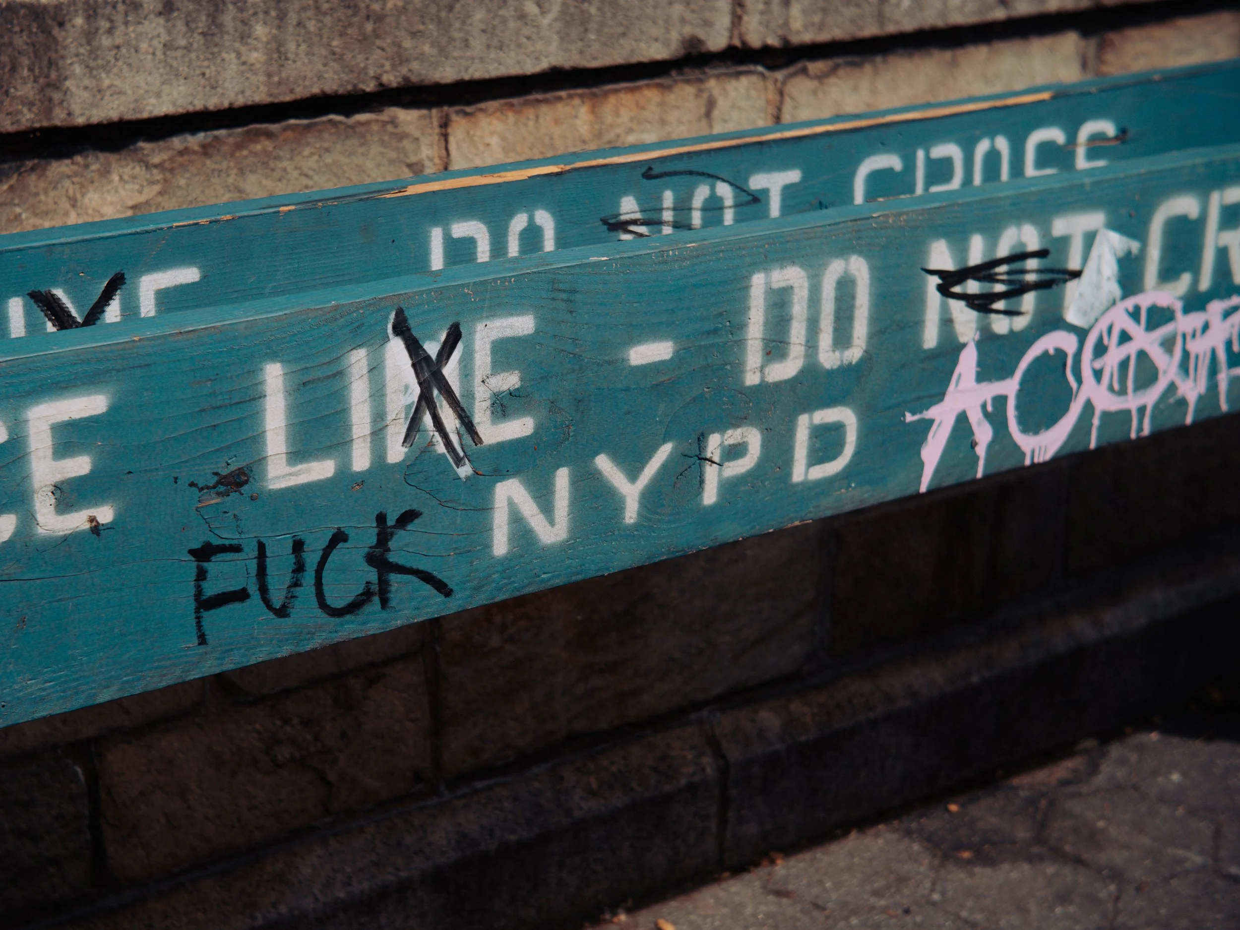 A blue wooden sign with the words "Fuck NYPD" spray painted on it. 
