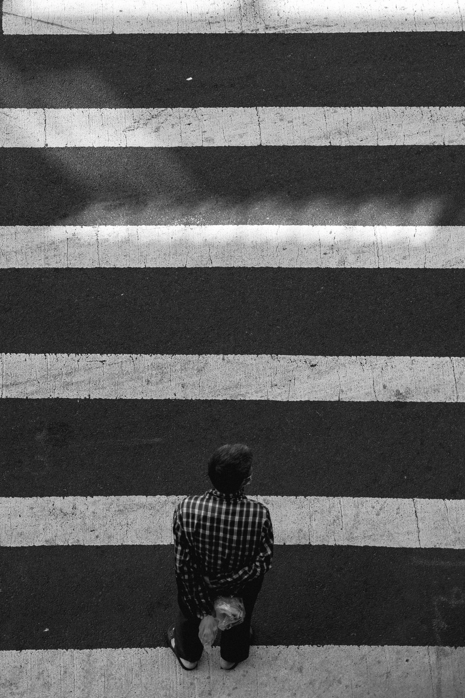 Overhead view of a man in a plaid shirt waiting at a crosswalk