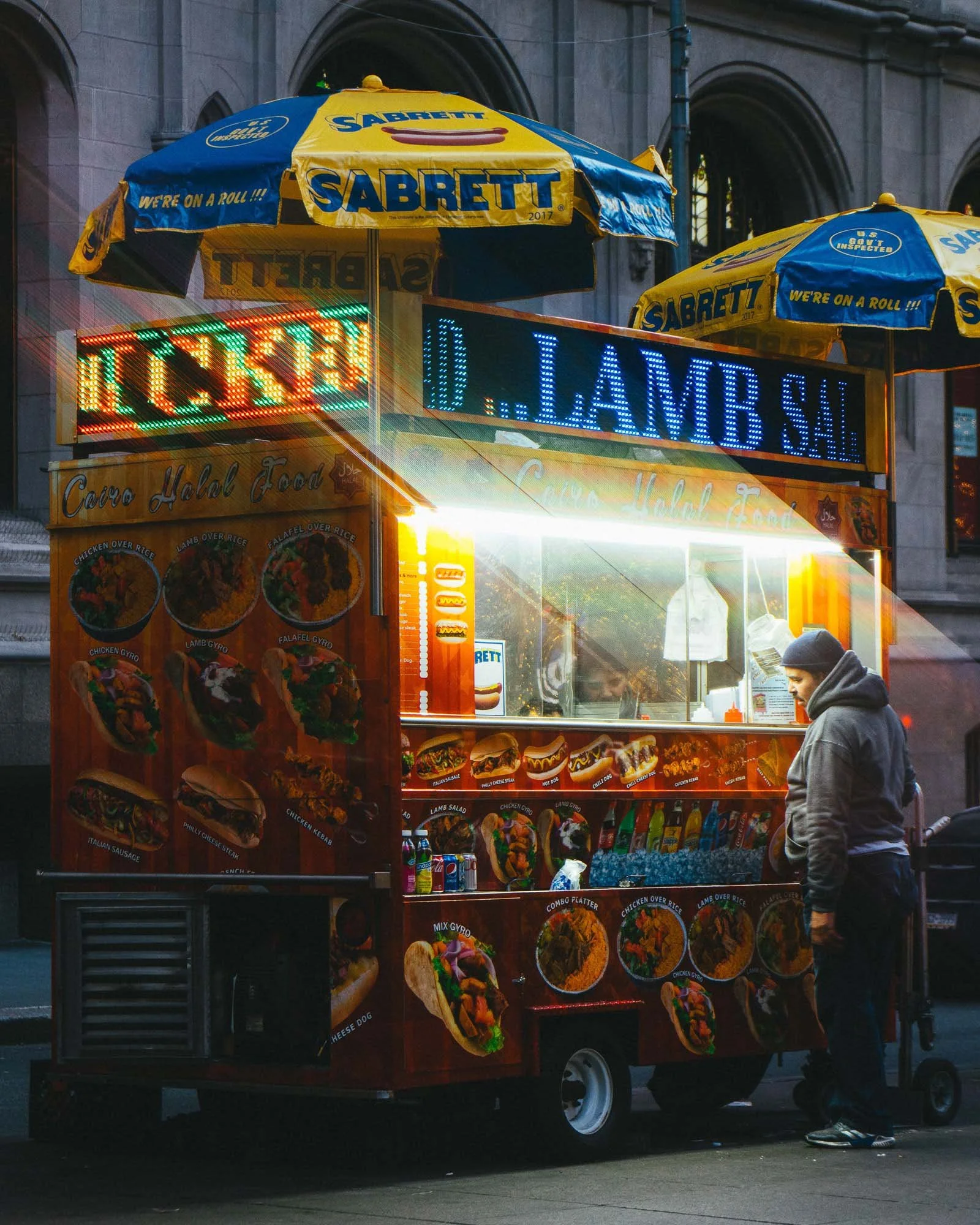 This print captures the street culture of New York City, with a man studying the menu of a food vendor under the warm glow of an overhead light.
